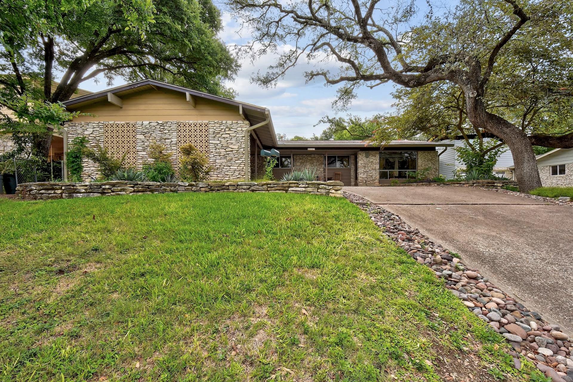 Mature trees shade a classic single-story stone e