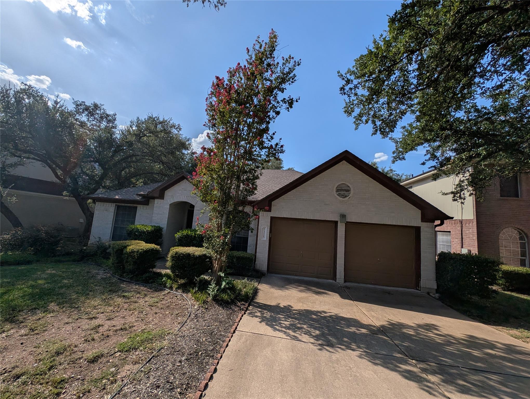Mature trees shade the concrete driveway leading 