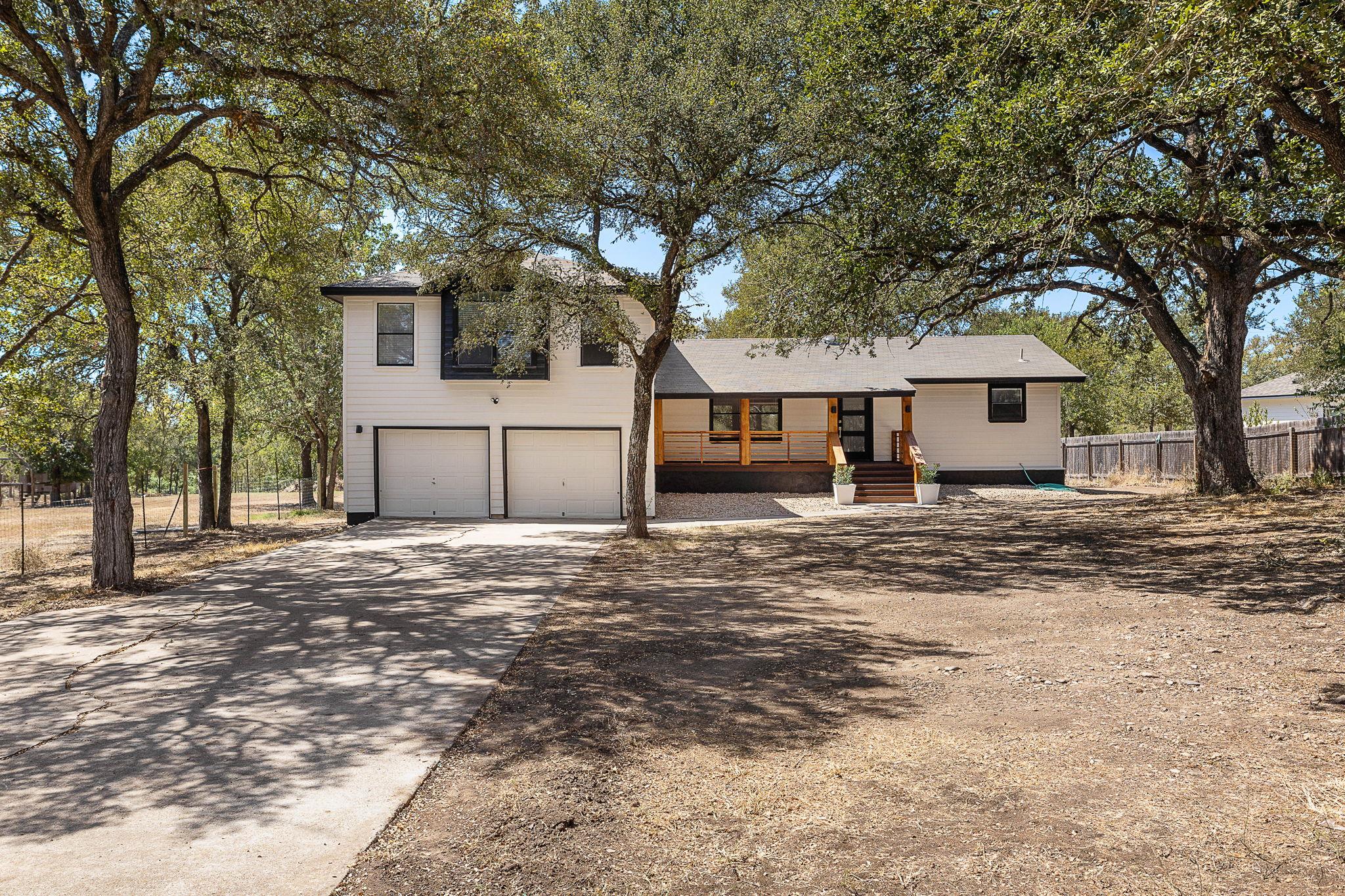 Mature trees shade the concrete driveway leading 