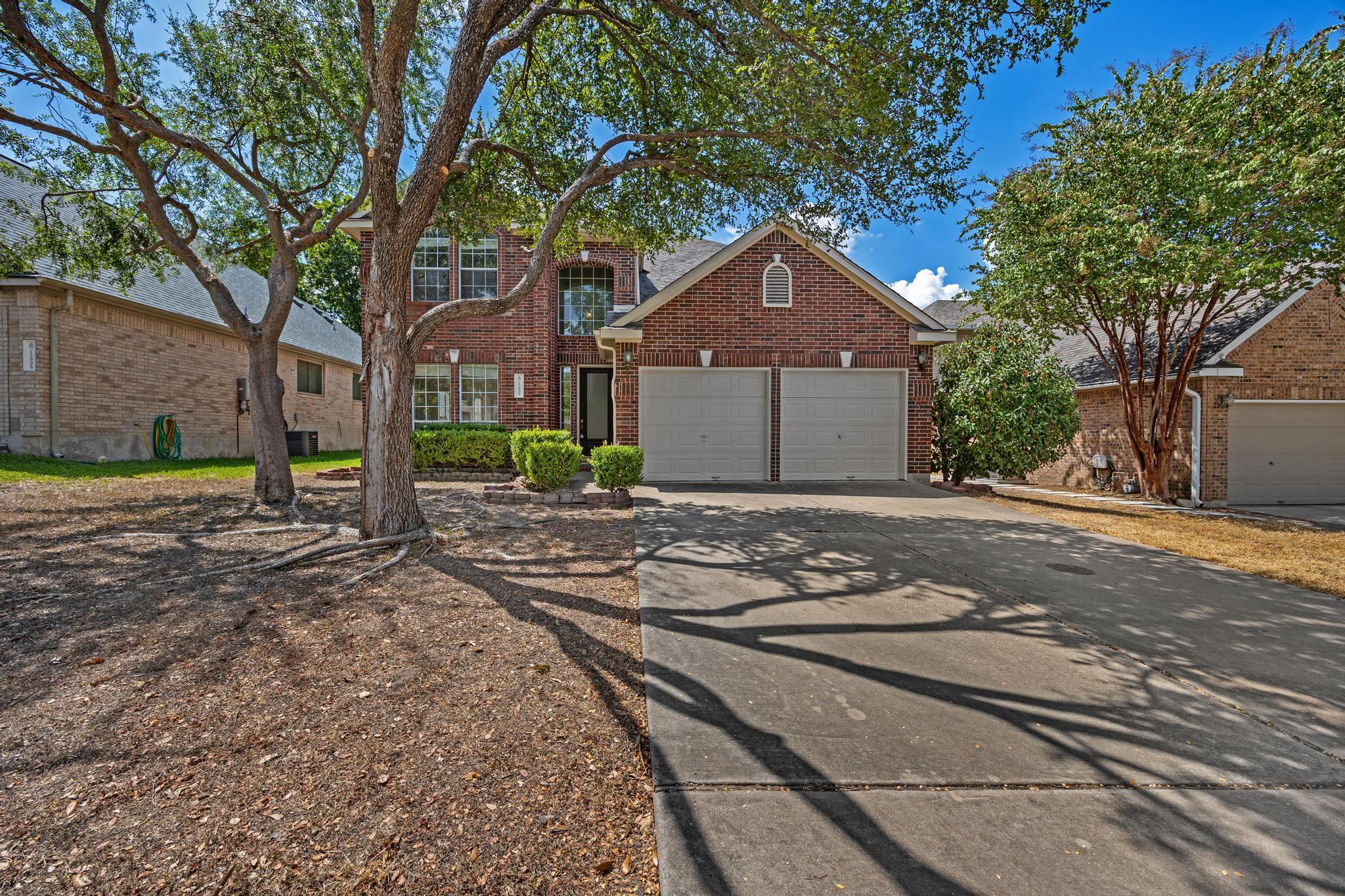 Mature shade trees frame the classic brick exteri