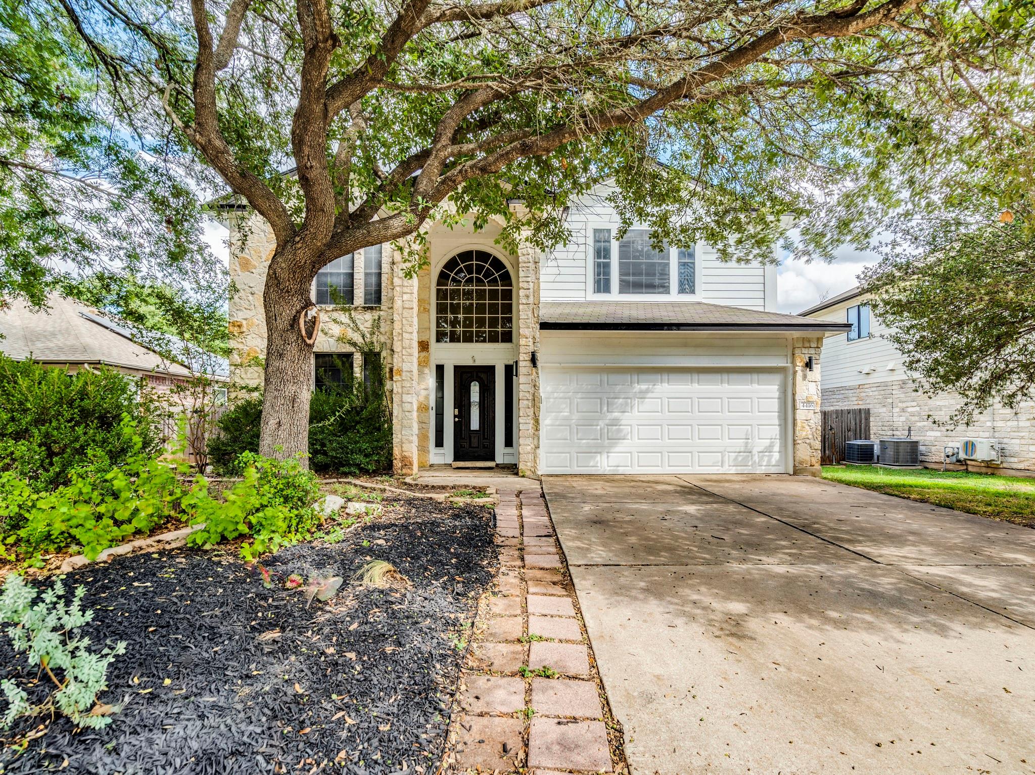 Mature trees frame a classic stone and siding fac