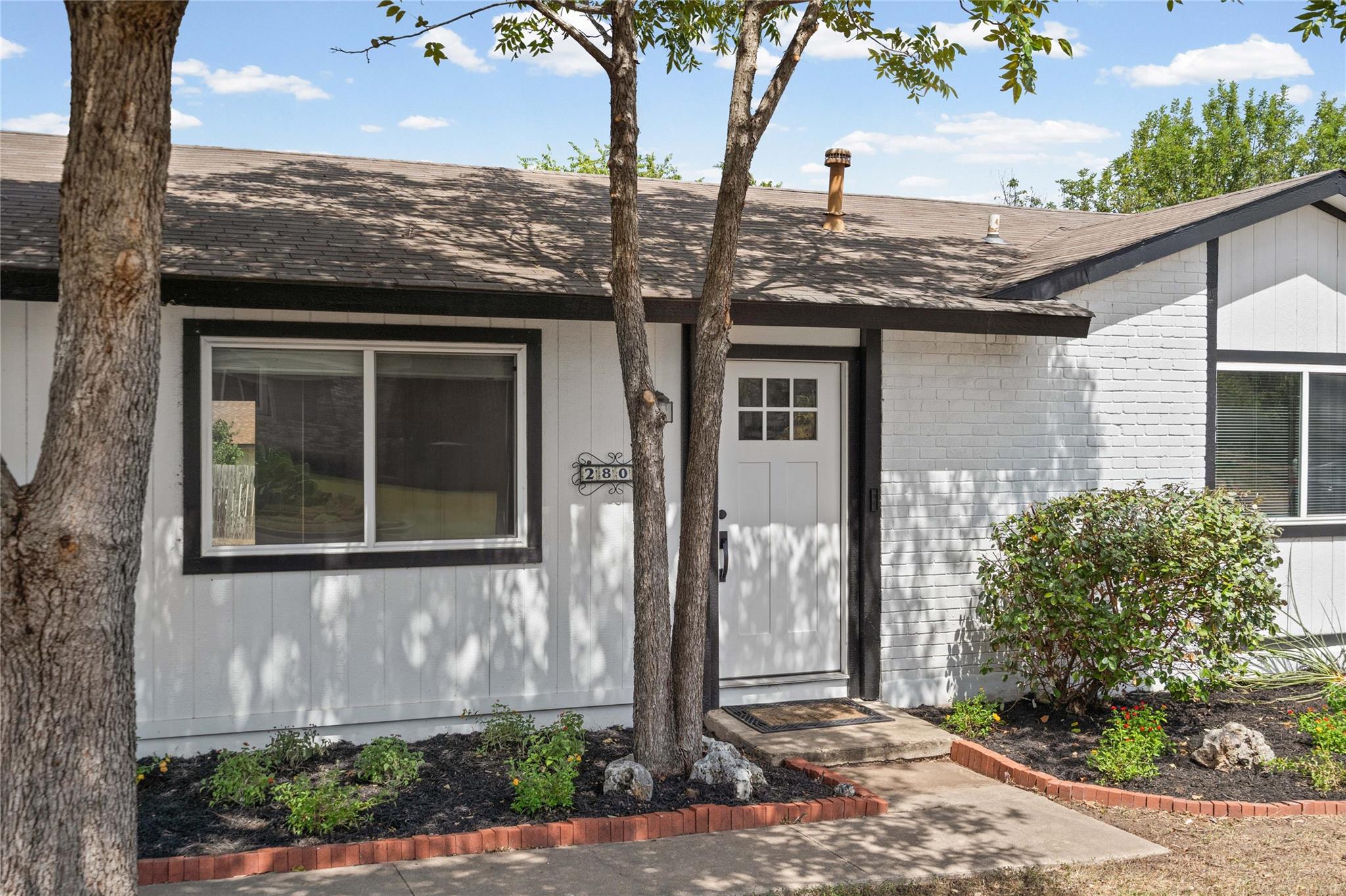 Mature trees shade a welcoming front entrance wit