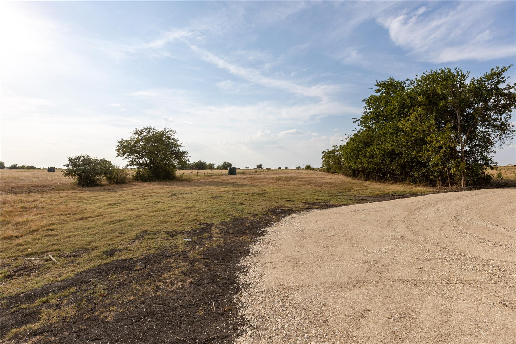 Mature trees and a gravel driveway frame the expa