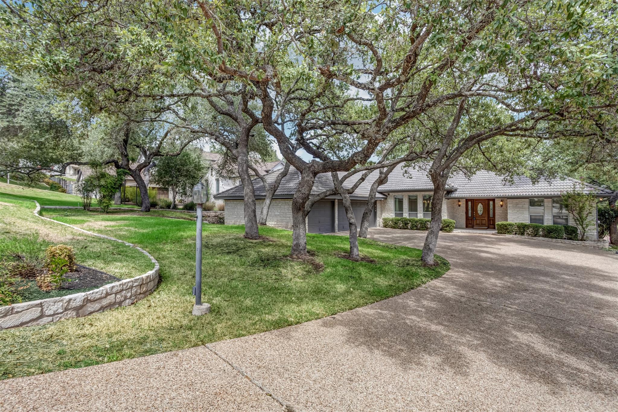 Mature oak trees frame a sweeping concrete drivew