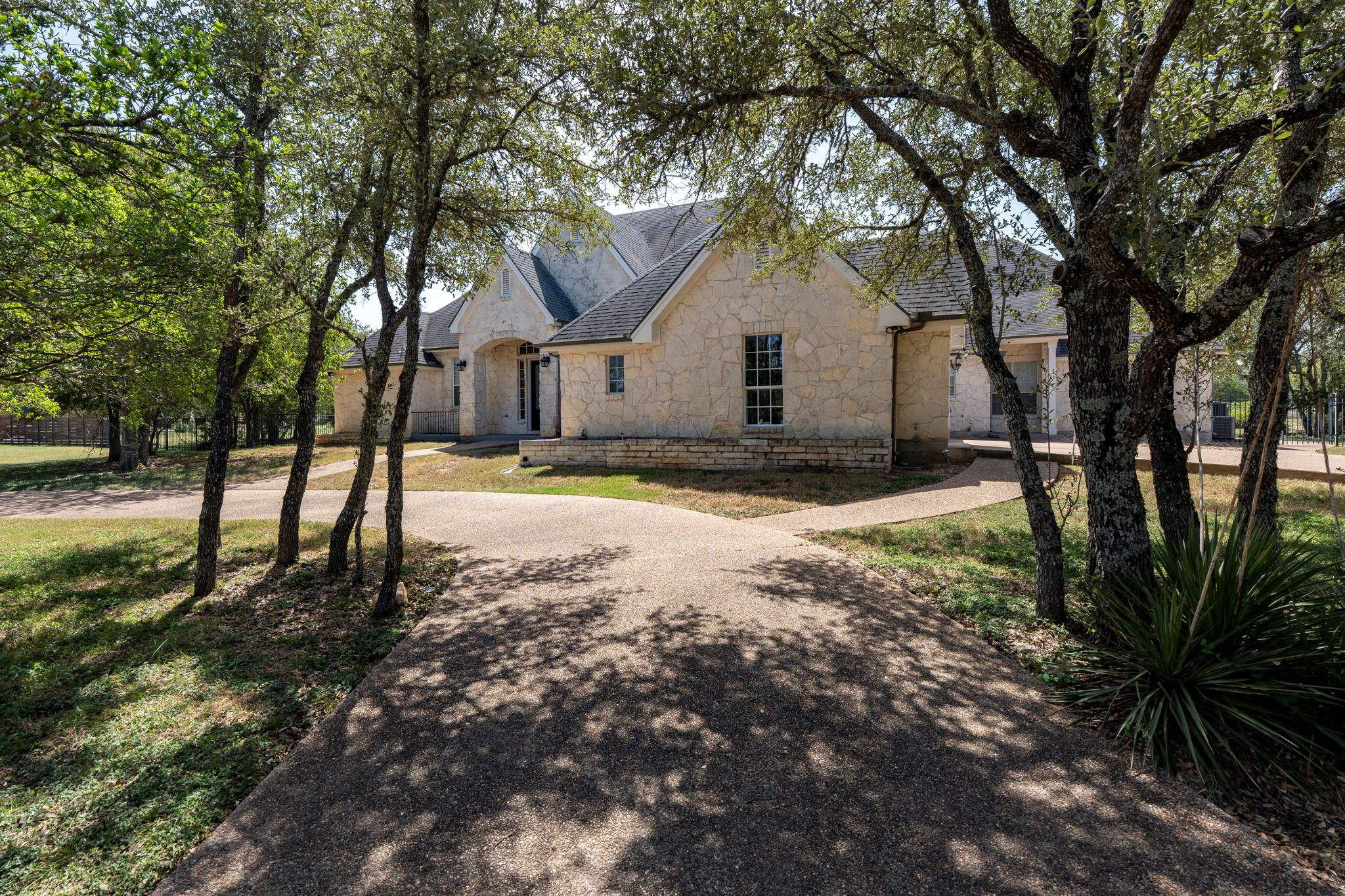 Mature trees shade the concrete driveway leading 