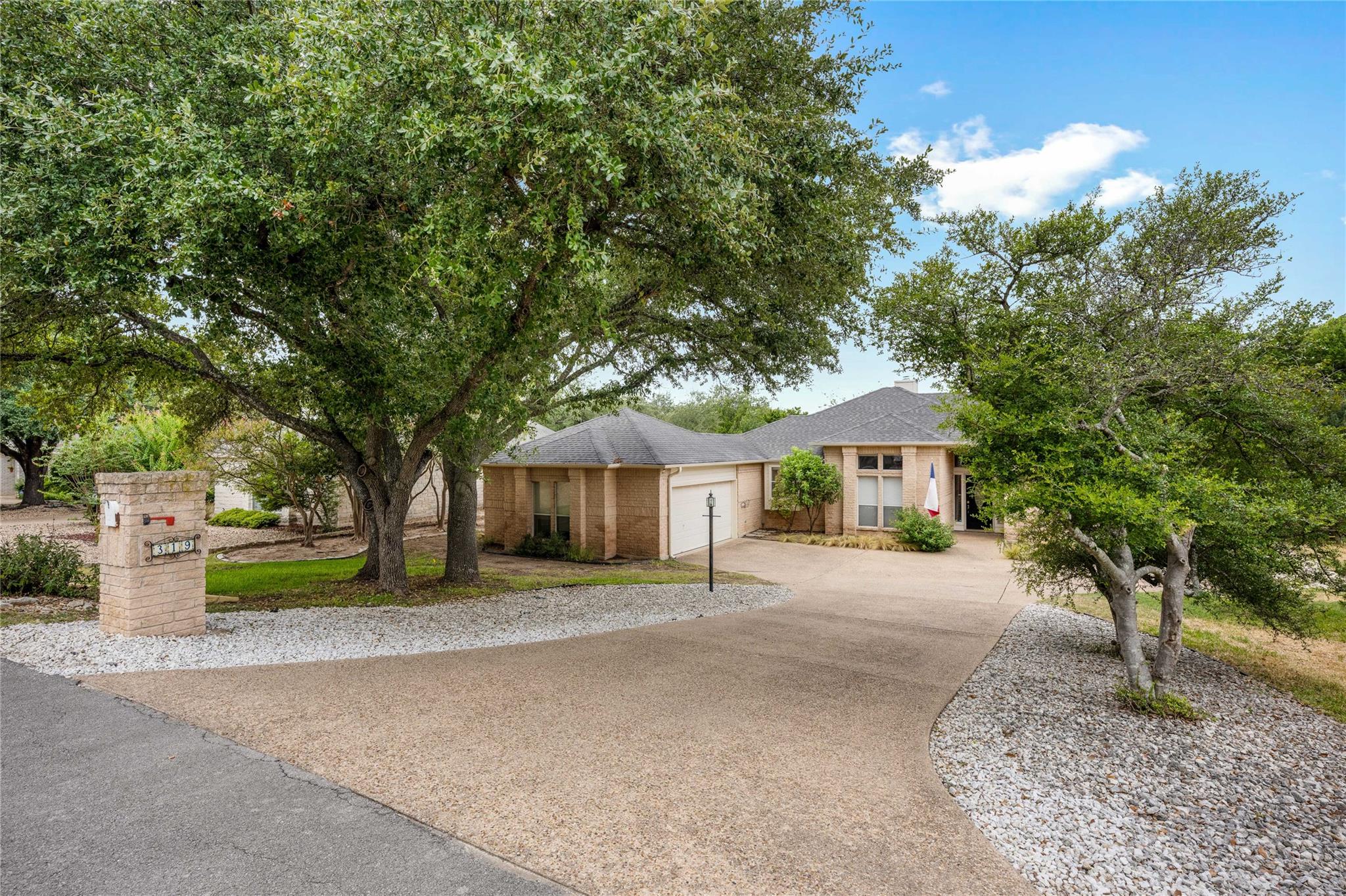 Mature oak trees frame the paved driveway leading