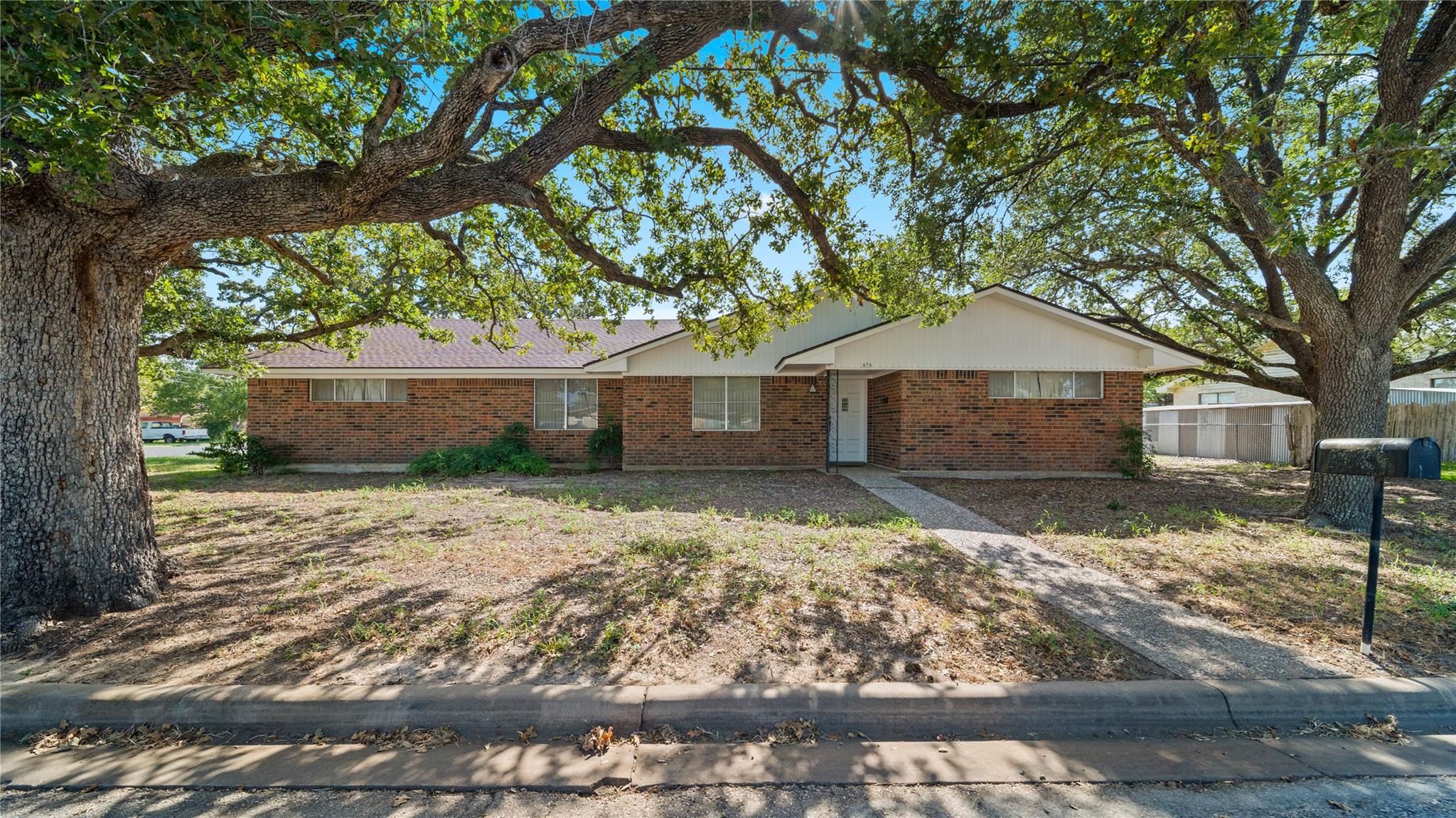 Mature oak trees frame the brick facade of this c