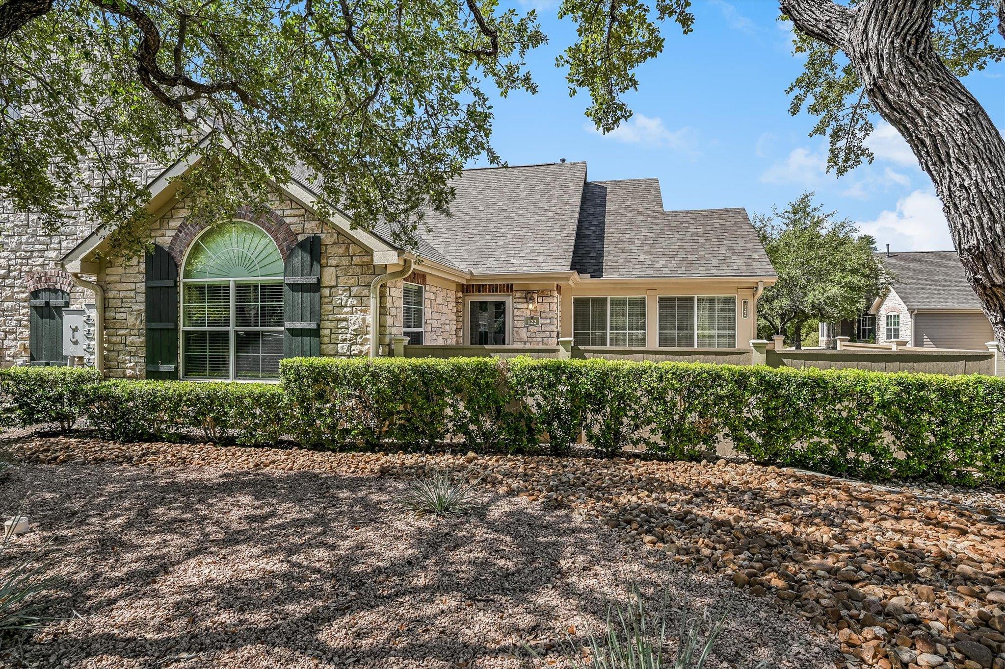 Mature shade trees and manicured hedging frame th