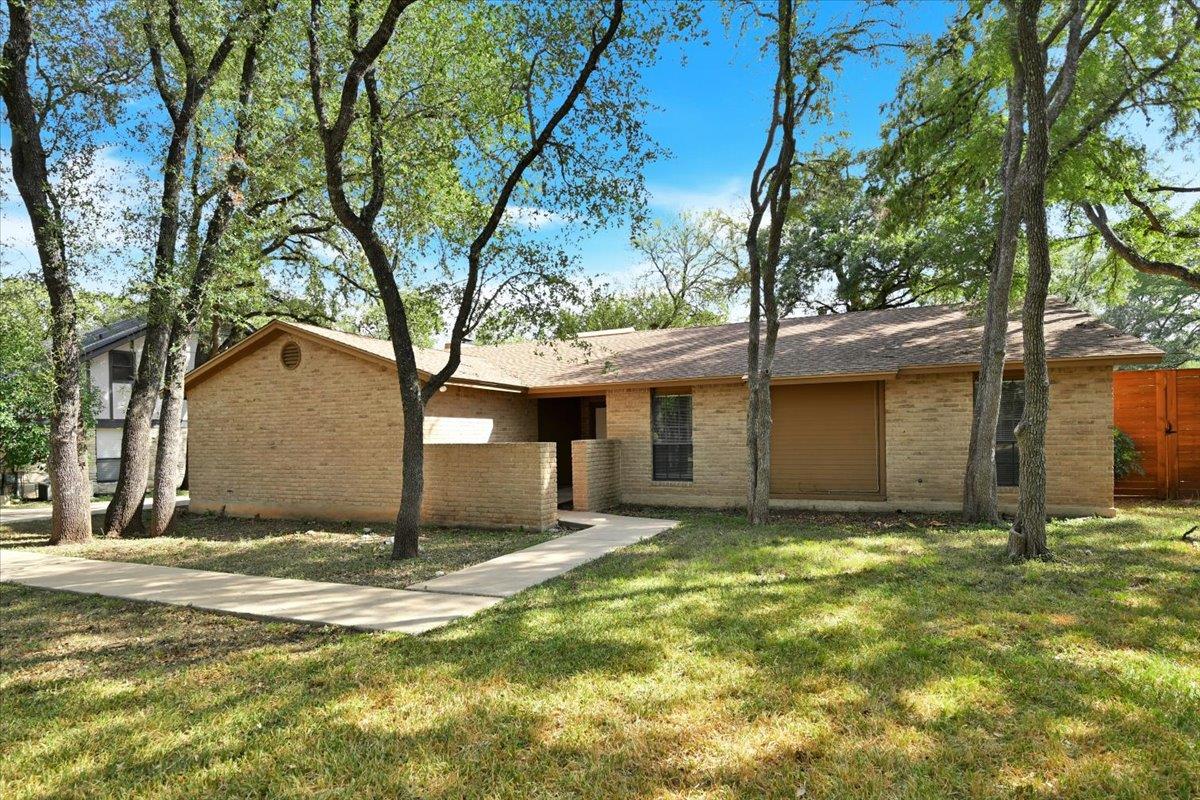 Mature trees shade a classic brick ranch-style ho