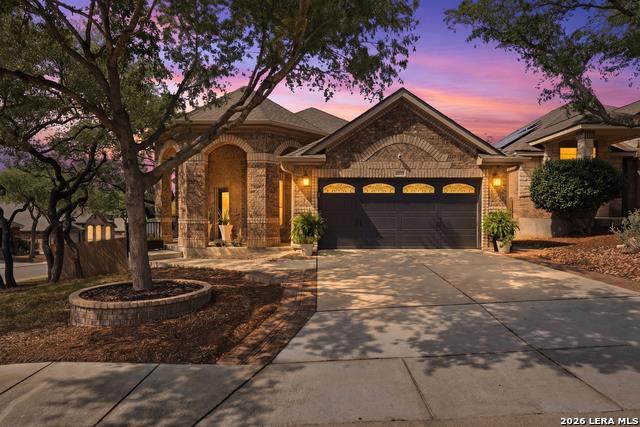 Mature trees shade a paved driveway leading to th