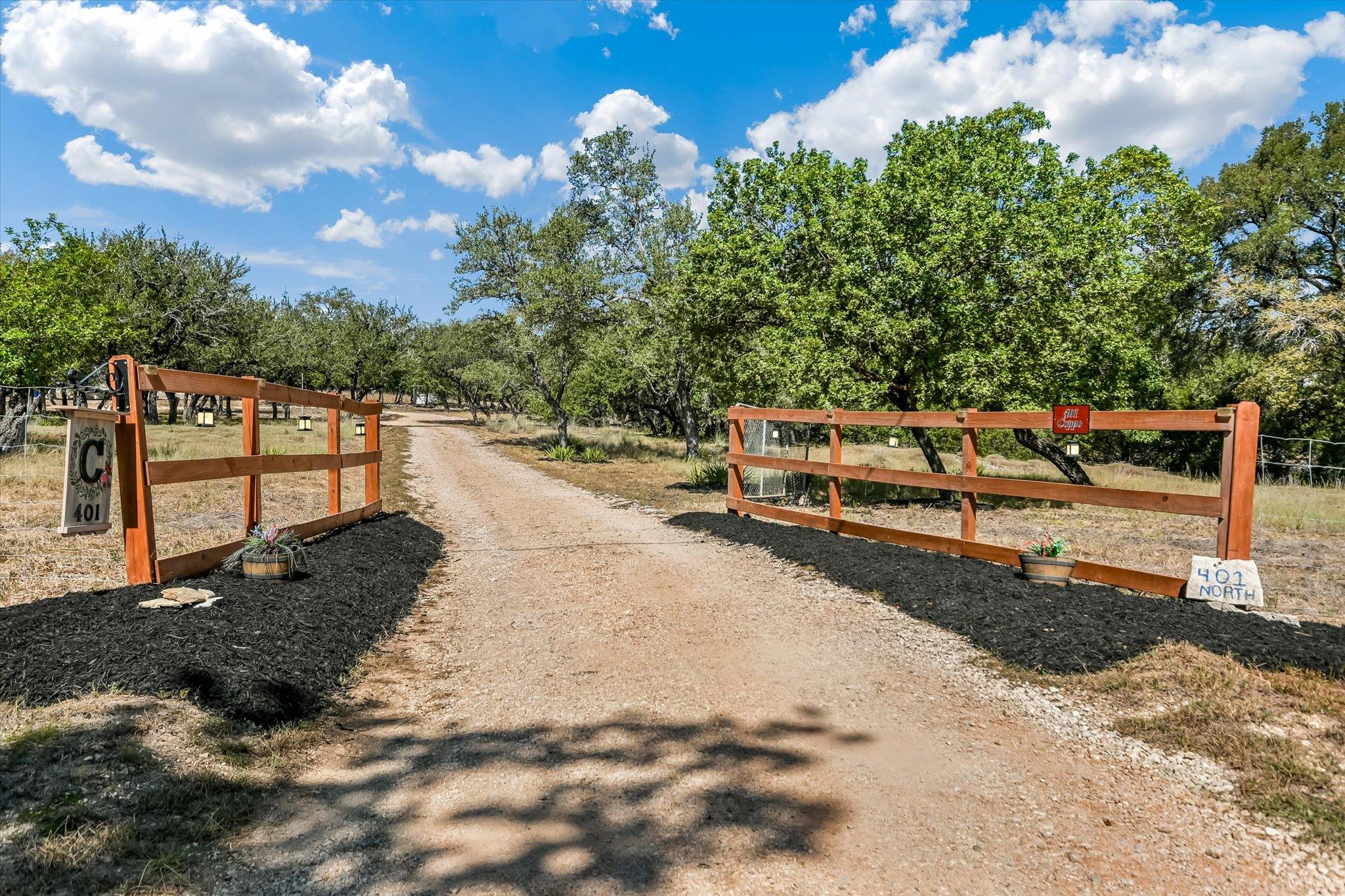 A rustic wood-fenced entrance opens to a long gra