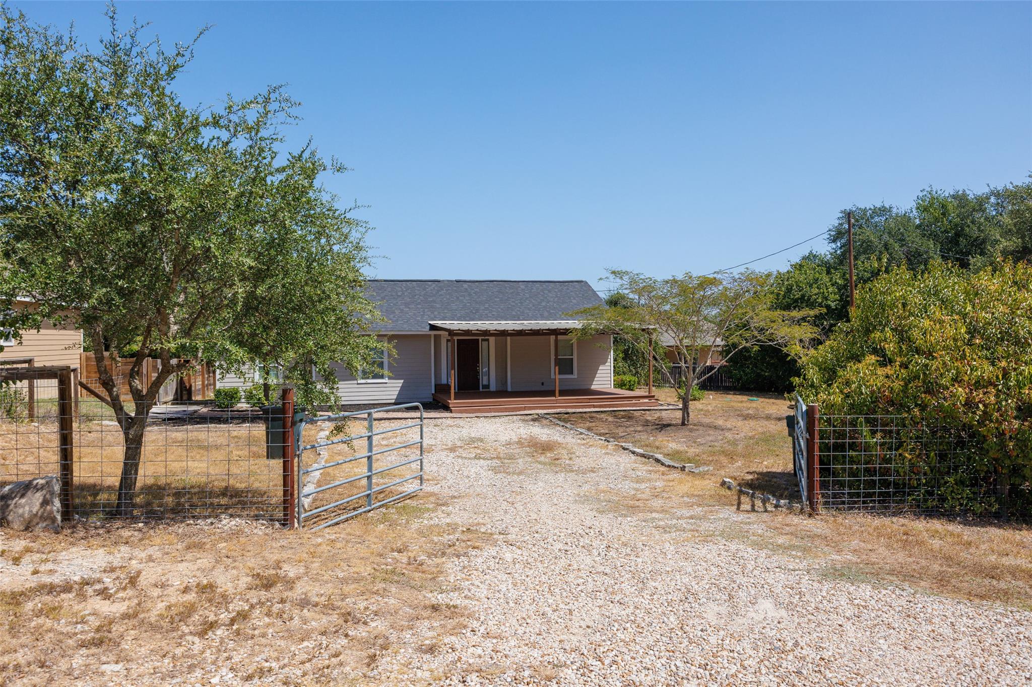 A gravel driveway leads through gated fencing to 