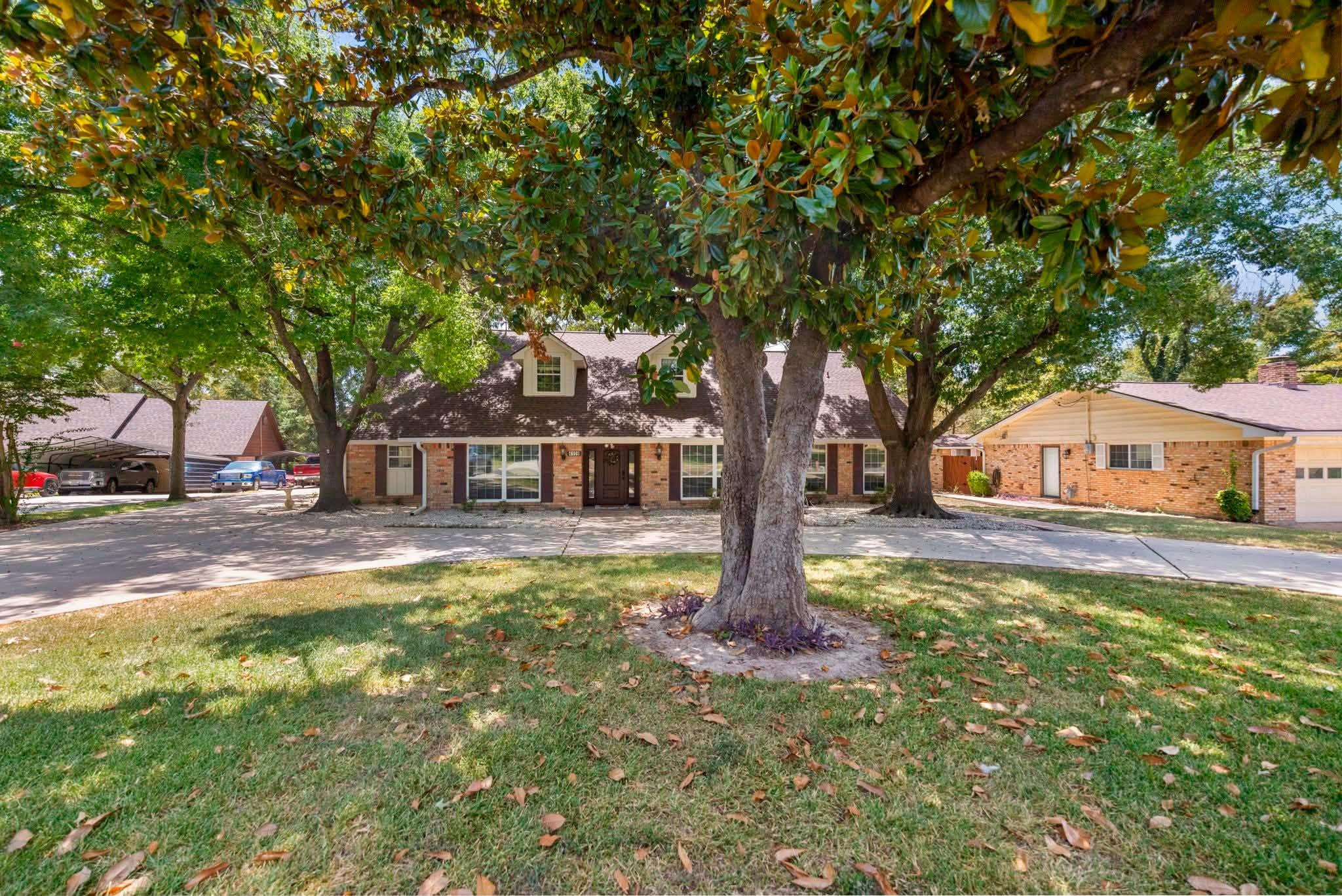 Mature trees shade a welcoming front lawn and cla