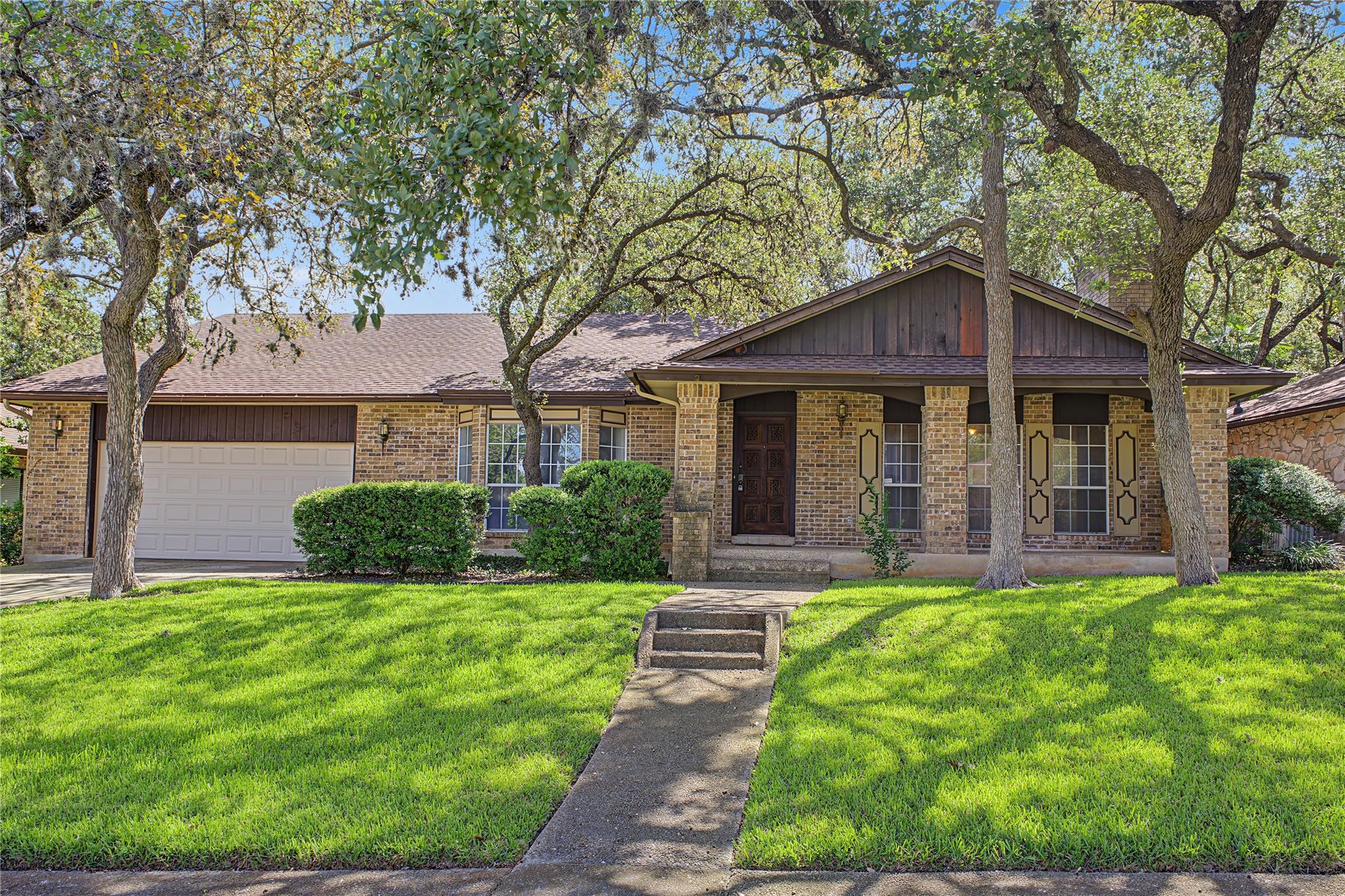 Mature shade trees frame this classic brick and w