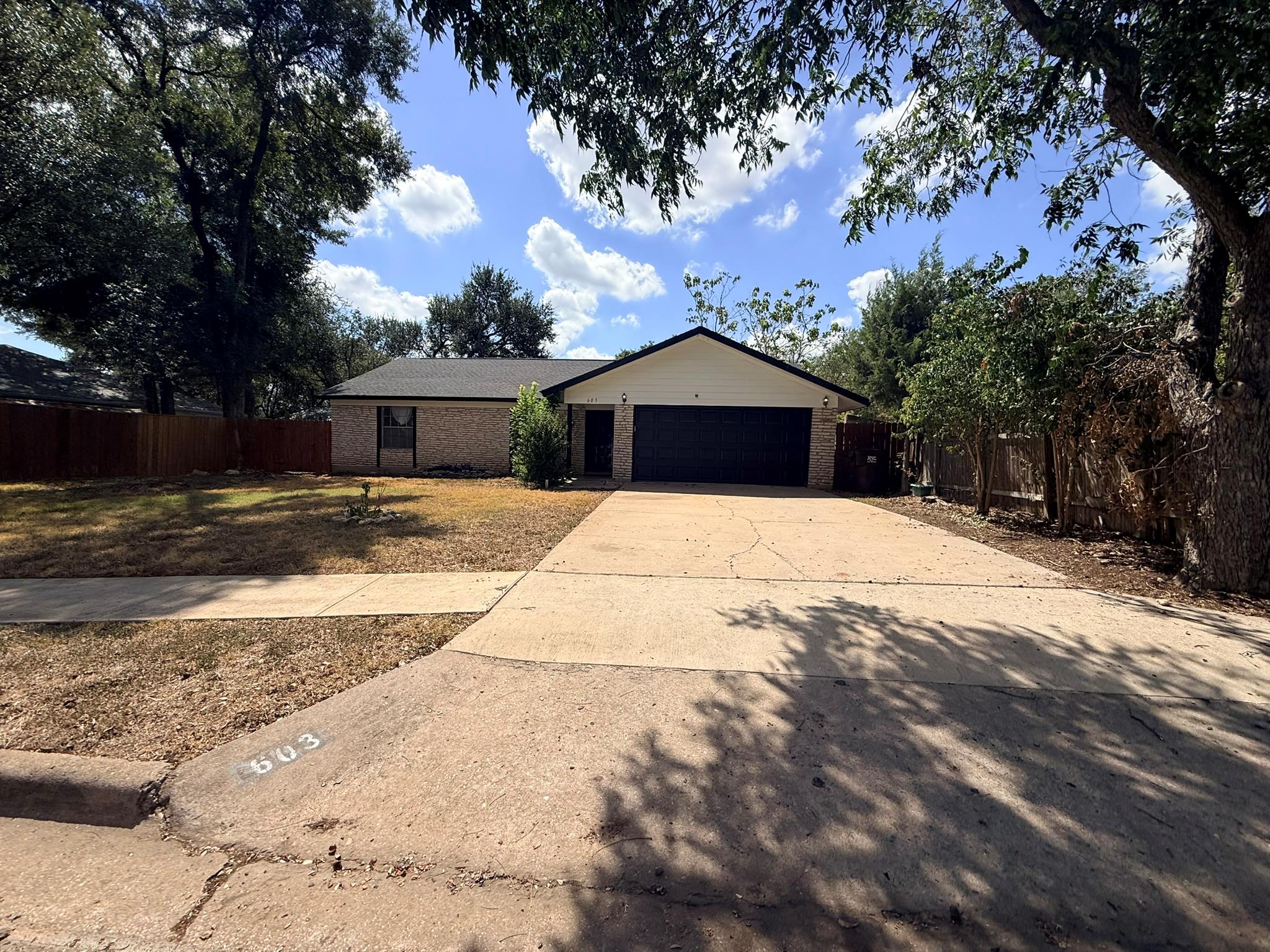 Mature trees shade a wide concrete driveway leadi