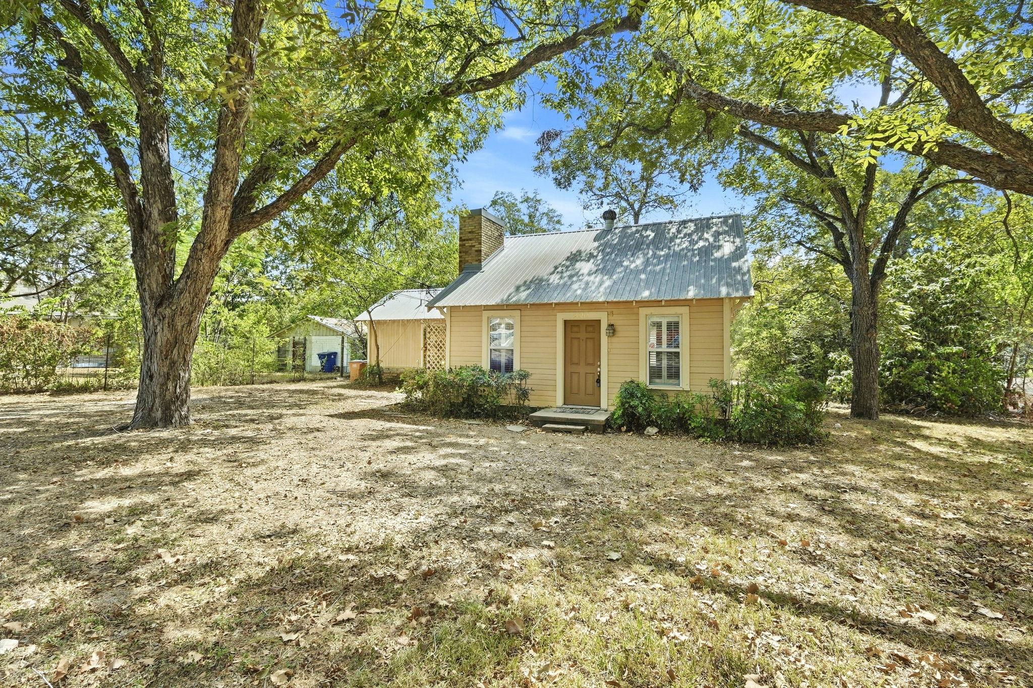Mature trees frame a charming cottage featuring a