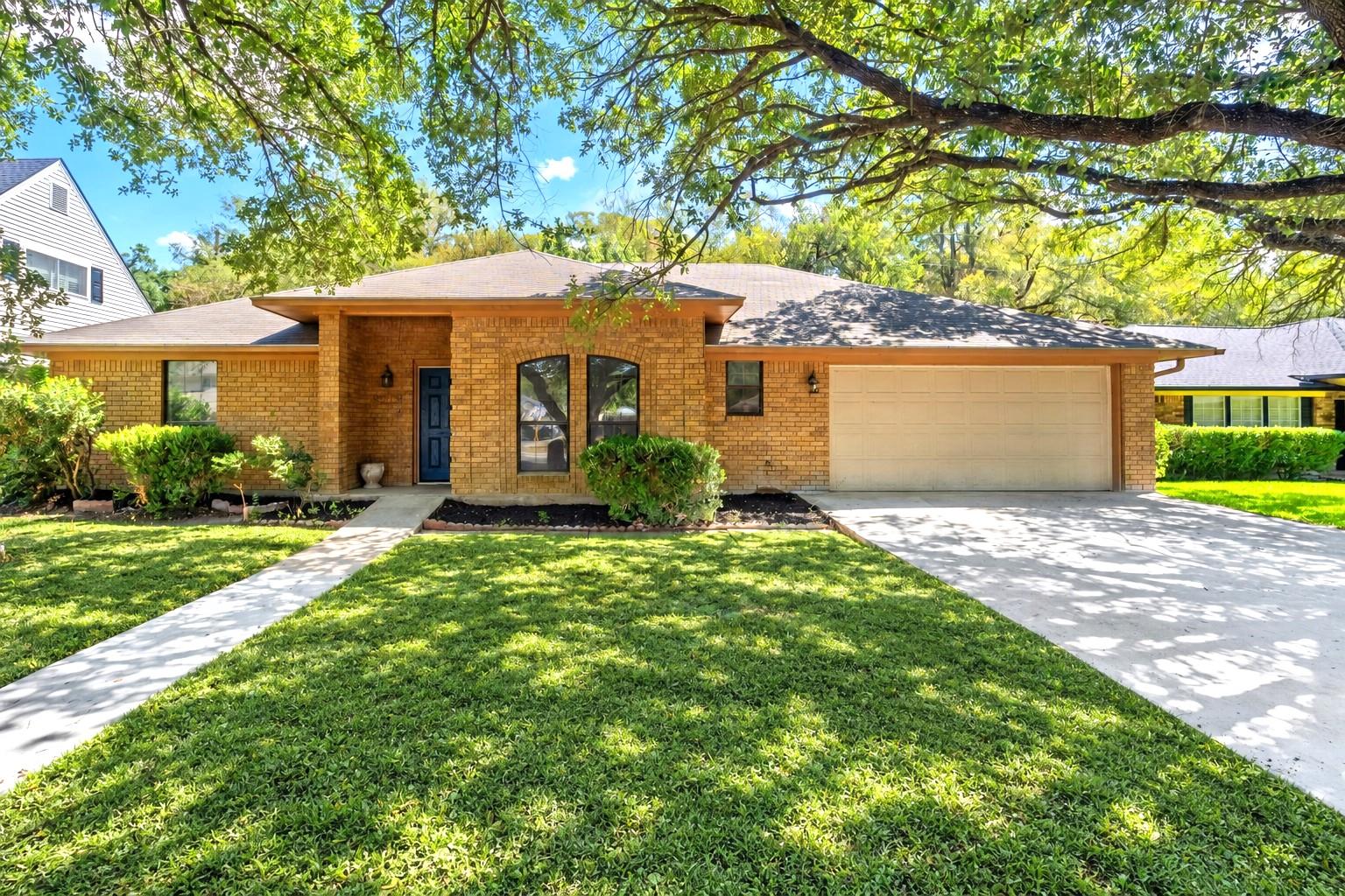 Mature shade trees frame this classic brick singl