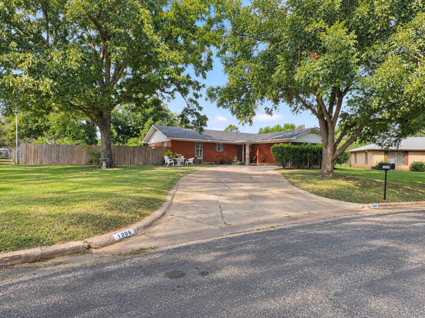 Mature shade trees frame a classic brick ranch-st