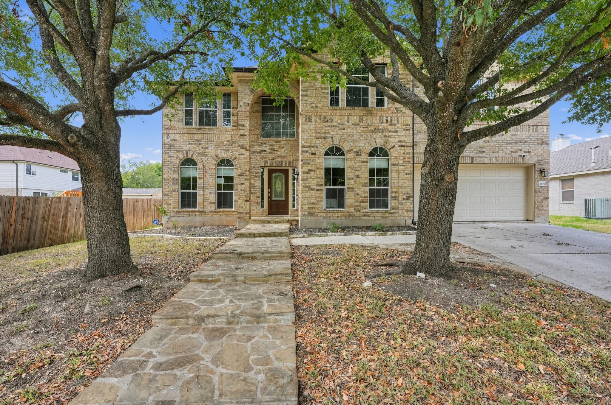 Mature shade trees frame a stone walkway leading 