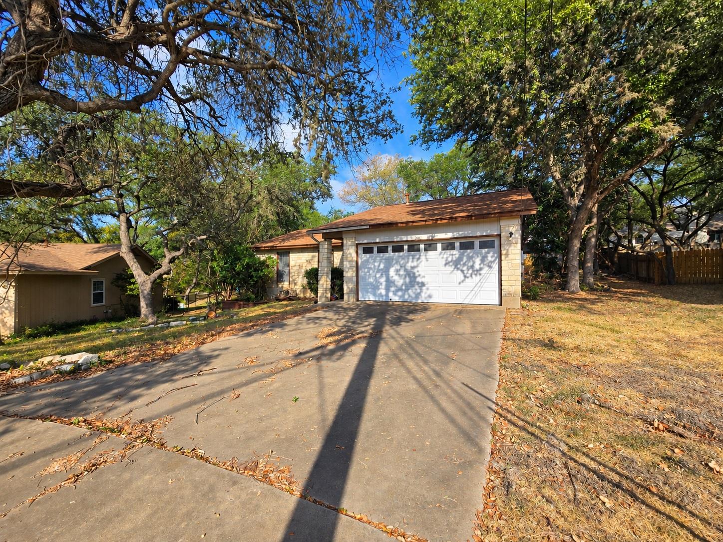 Mature trees frame the concrete driveway leading 