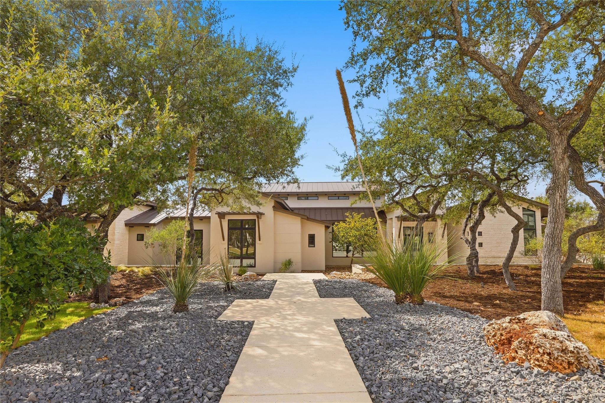 Mature oak trees frame a modern facade with a wel