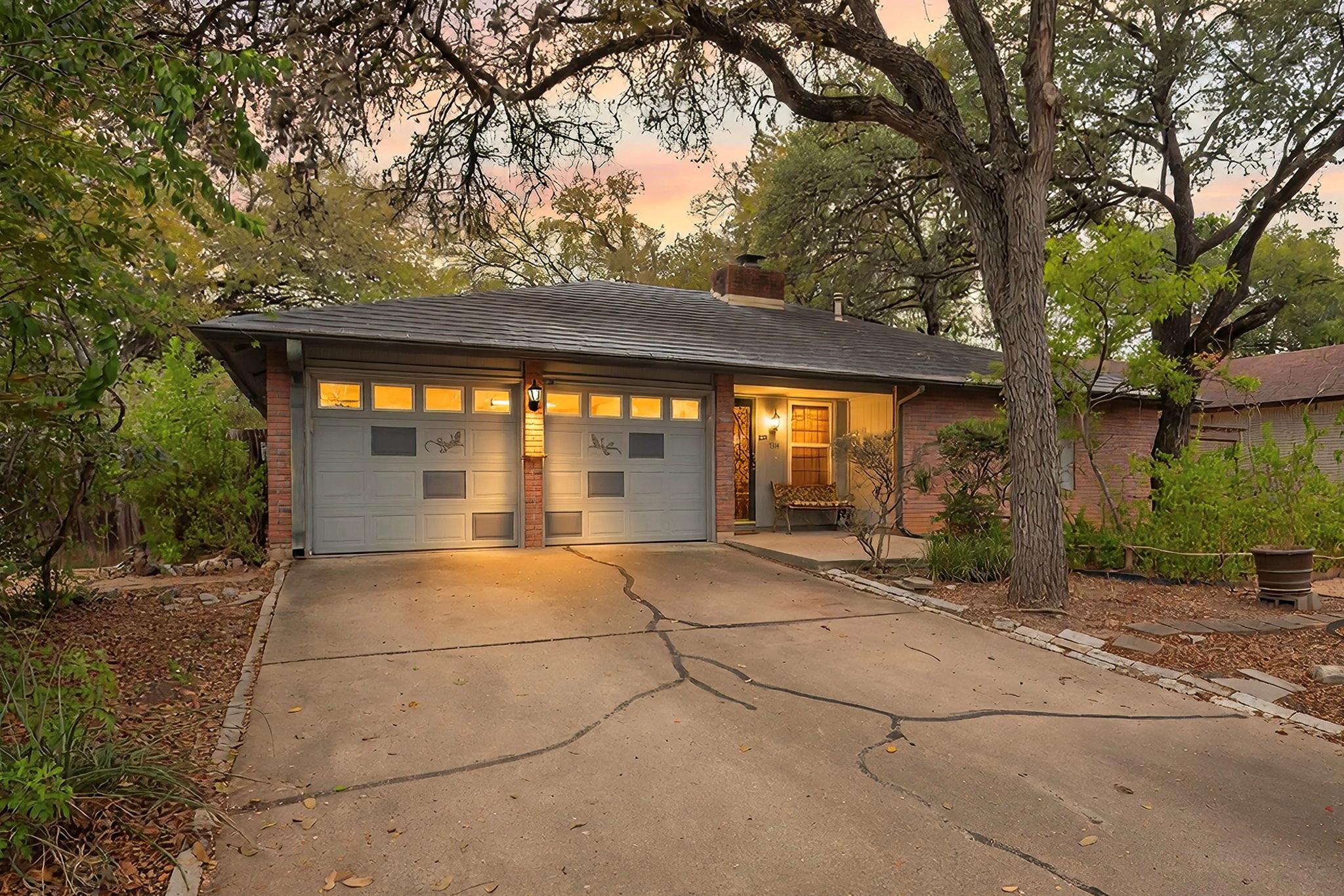 Mature trees shade the concrete driveway and bric