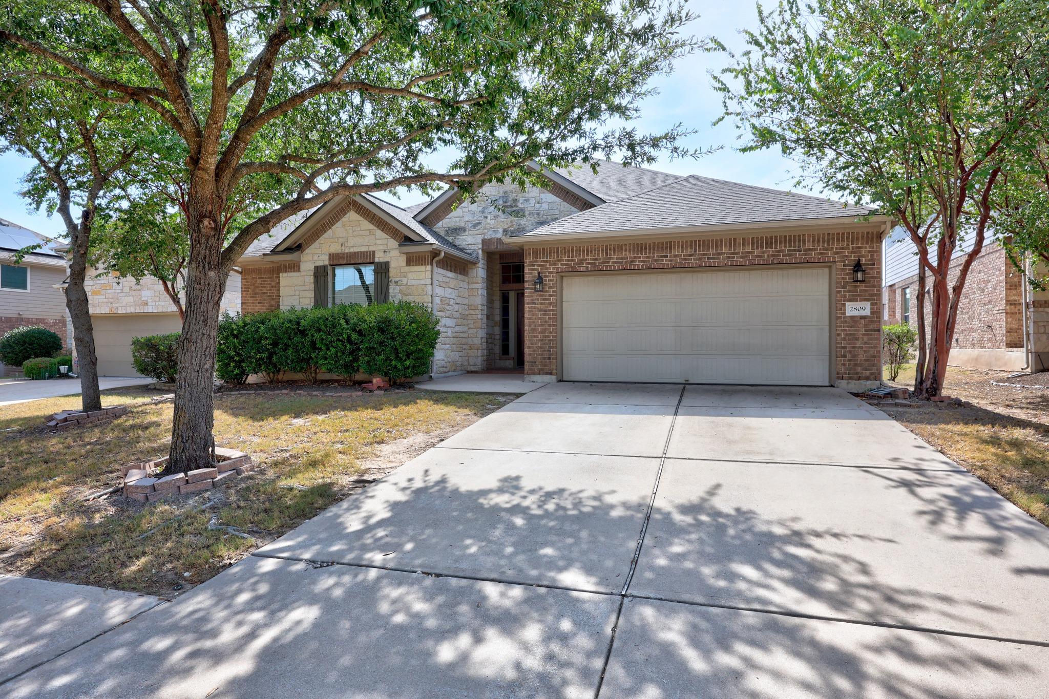 Mature trees shade the concrete driveway leading 