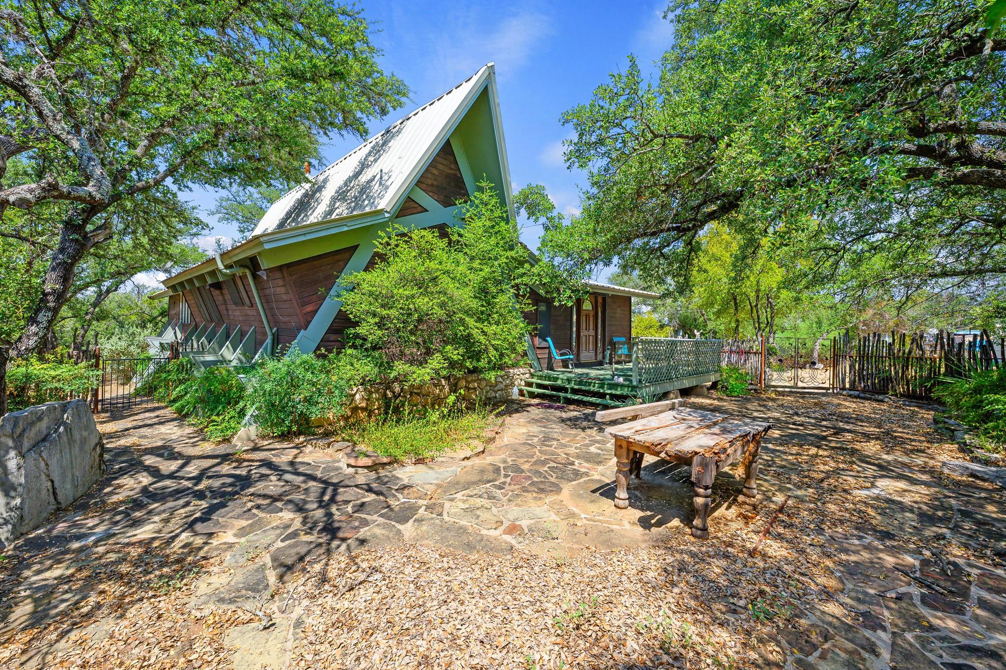 Mature trees shade a rustic stone patio leading t