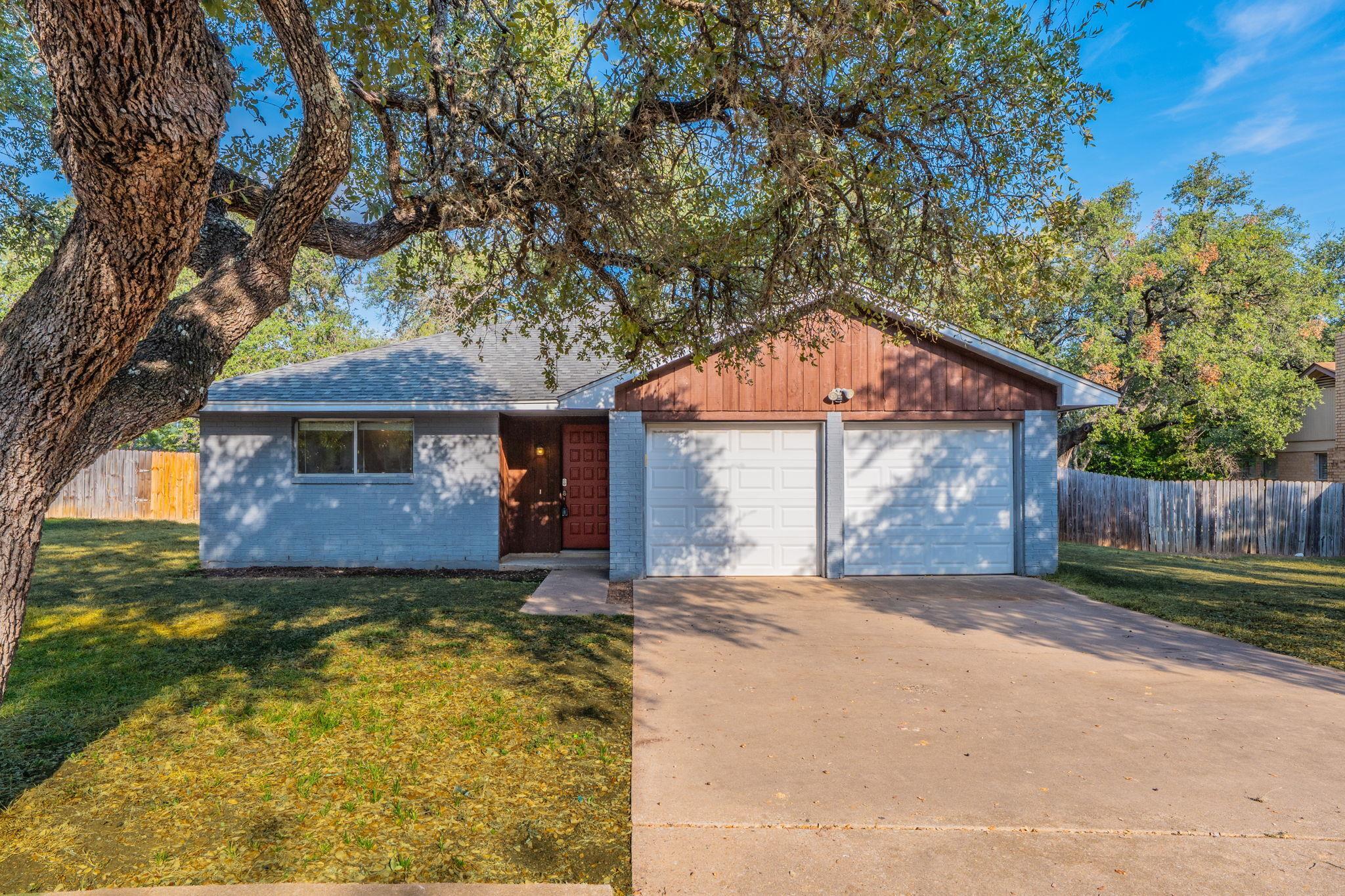 Mature shade trees frame the concrete driveway le