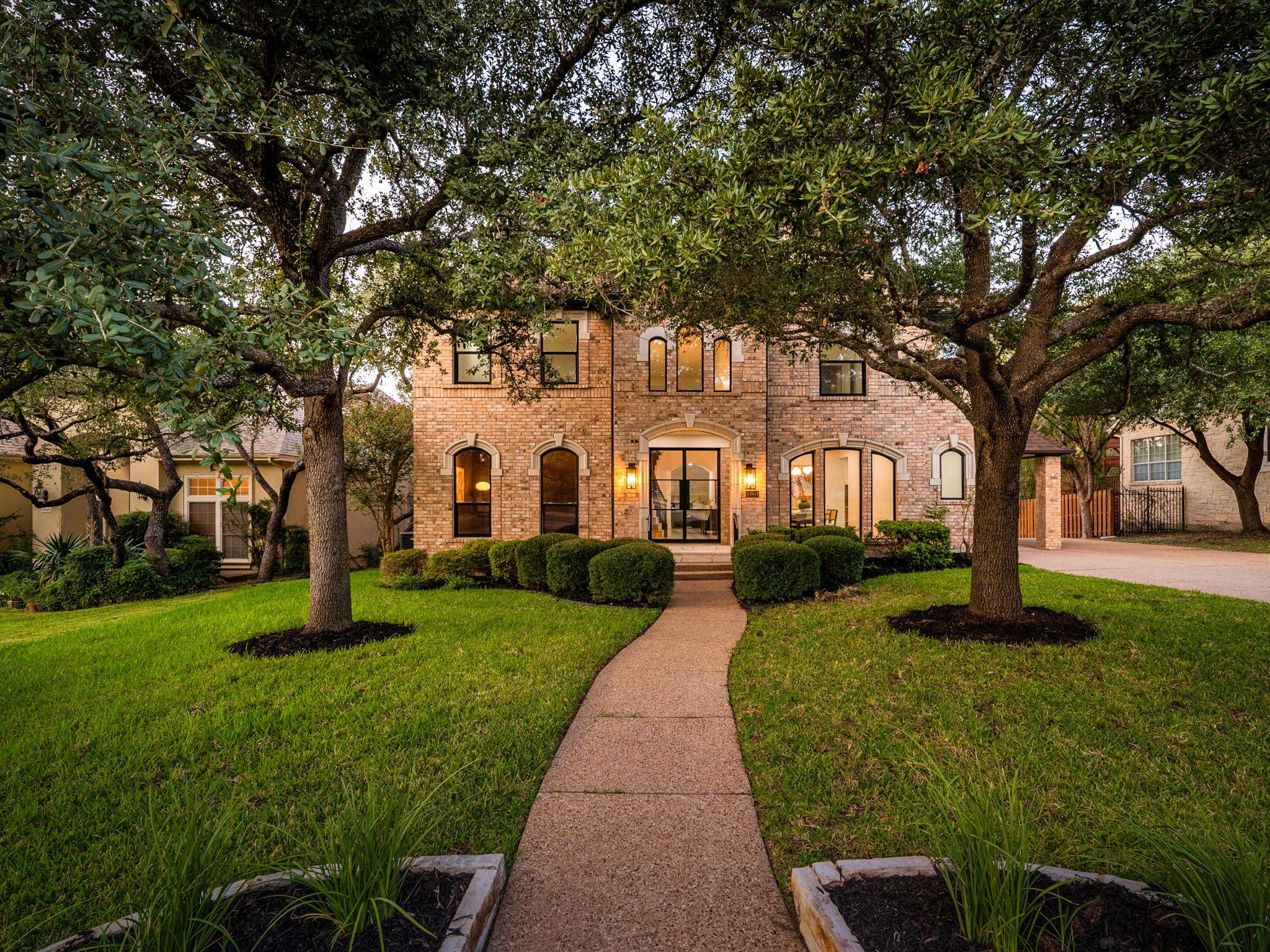 Mature trees shade the front lawn and stone walkw