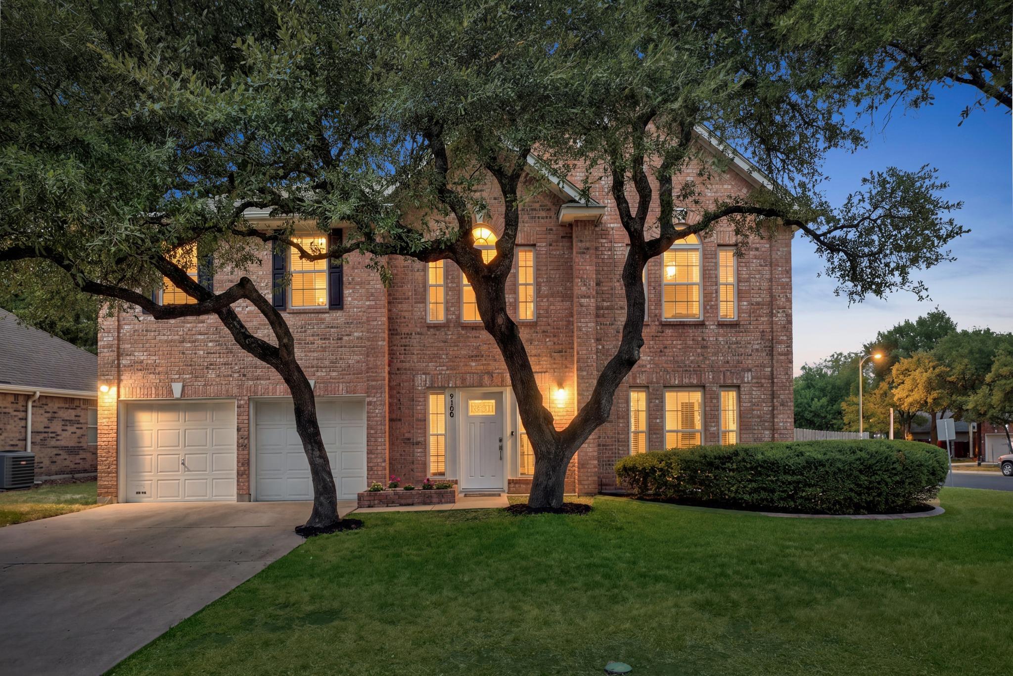 Mature shade trees and a concrete driveway lead t
