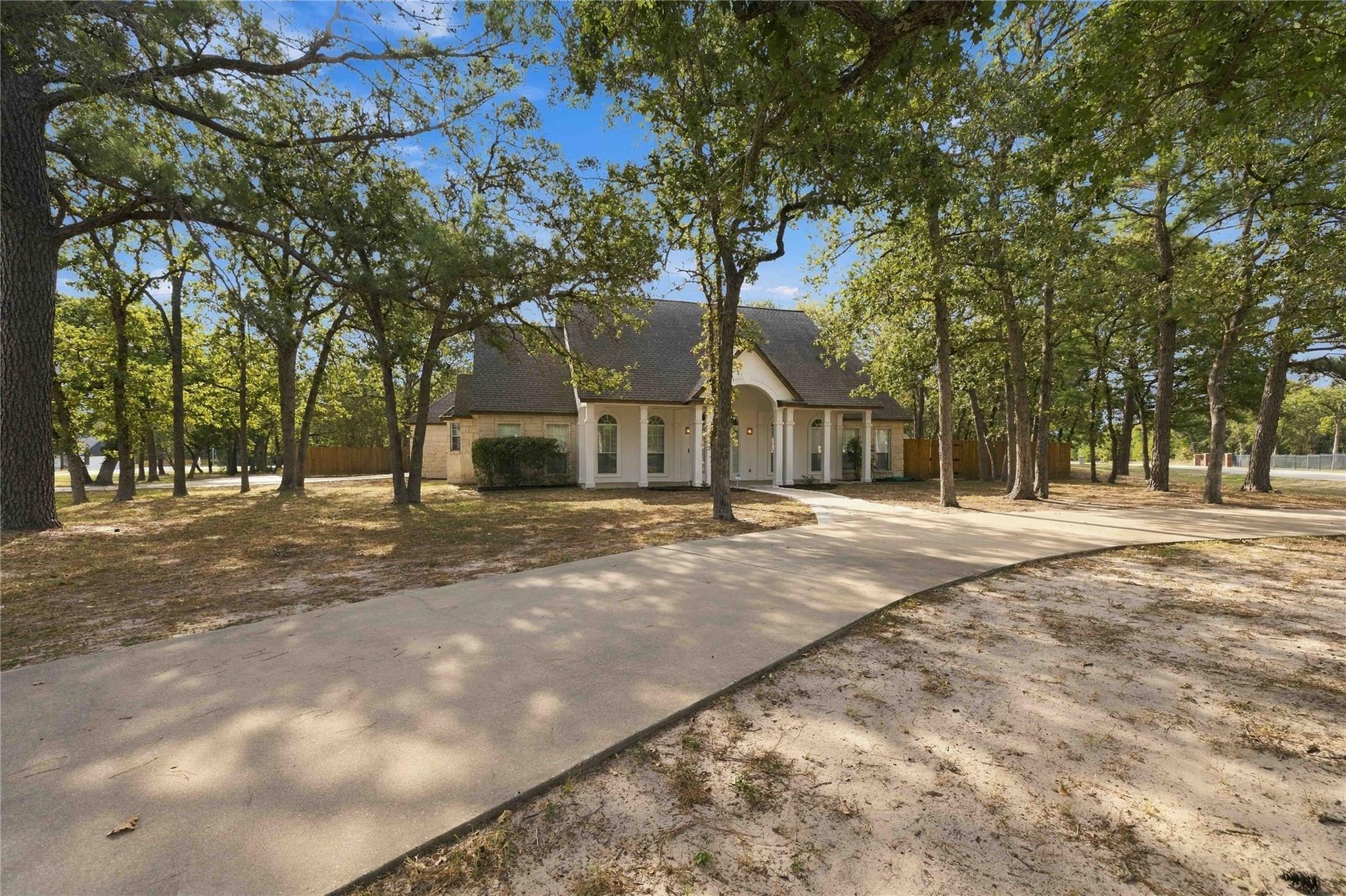 Mature trees frame a winding concrete driveway le