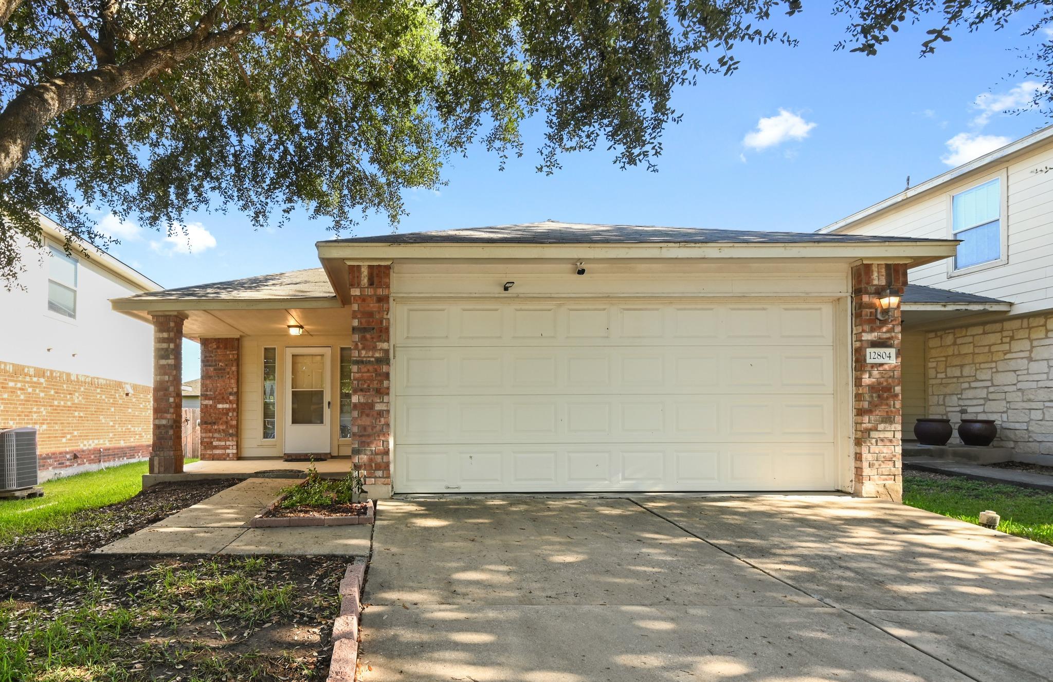 Mature trees shade the concrete driveway leading 