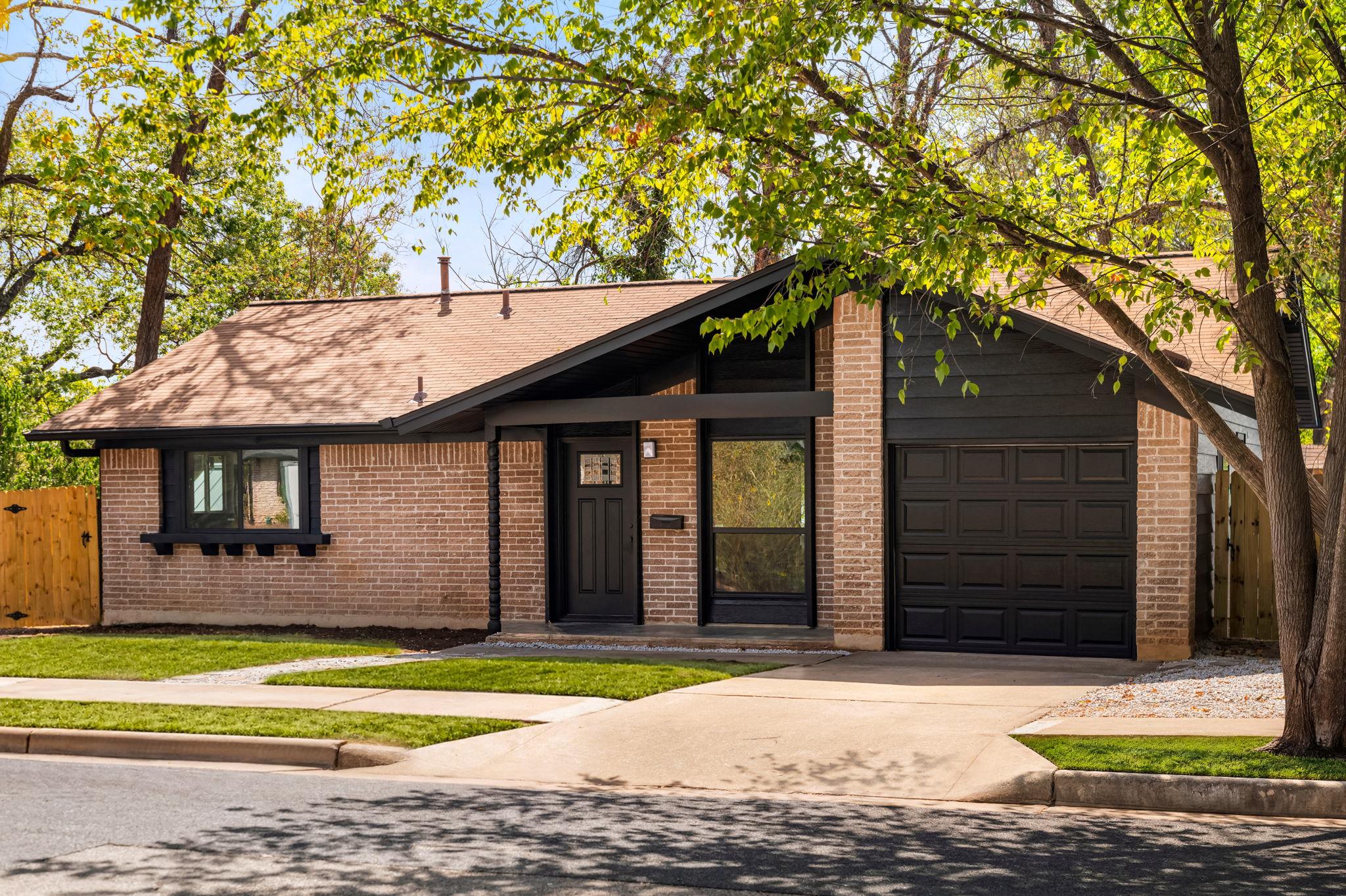 Mature trees frame a mid-century brick ranch home