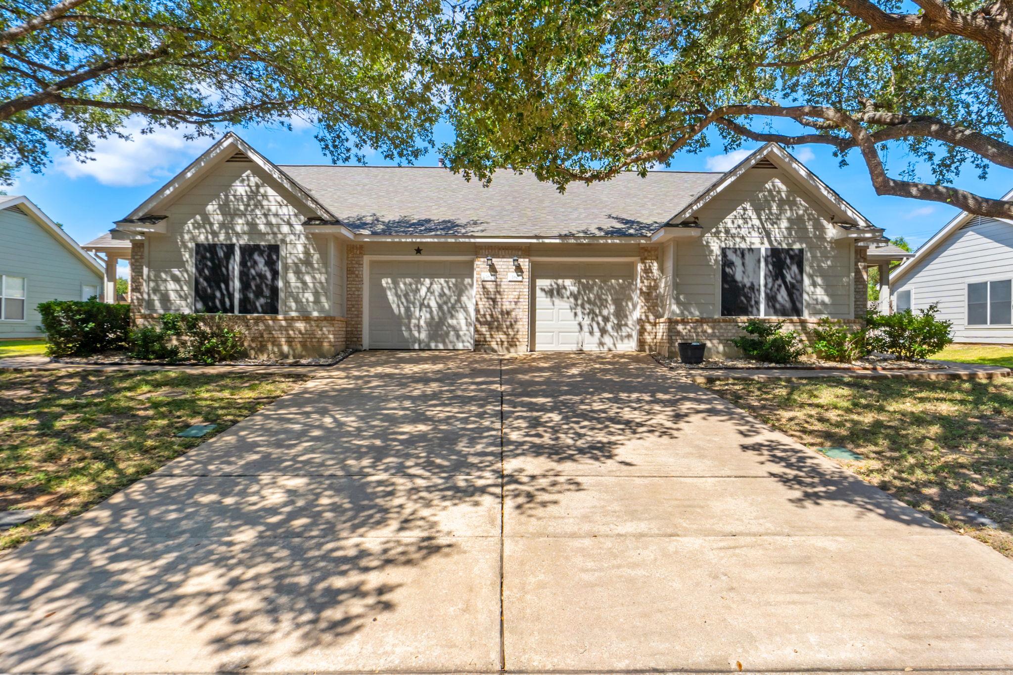 Mature shade trees frame a wide concrete driveway