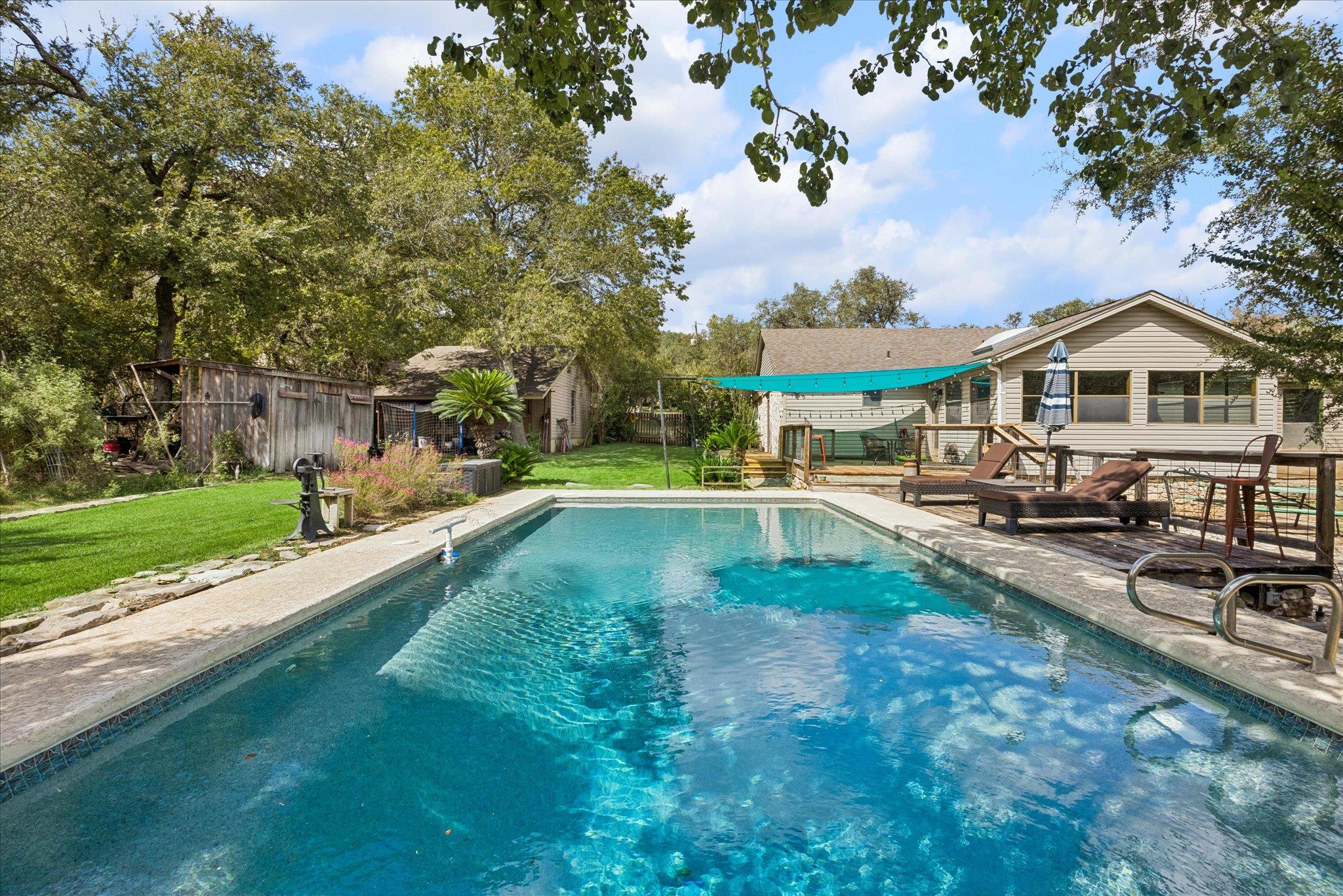 Mature trees frame a sparkling inground pool and 