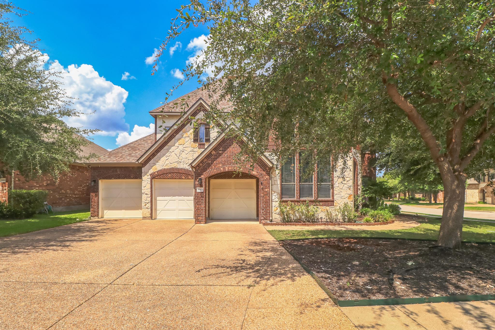 Mature trees frame a classic brick and stone faca
