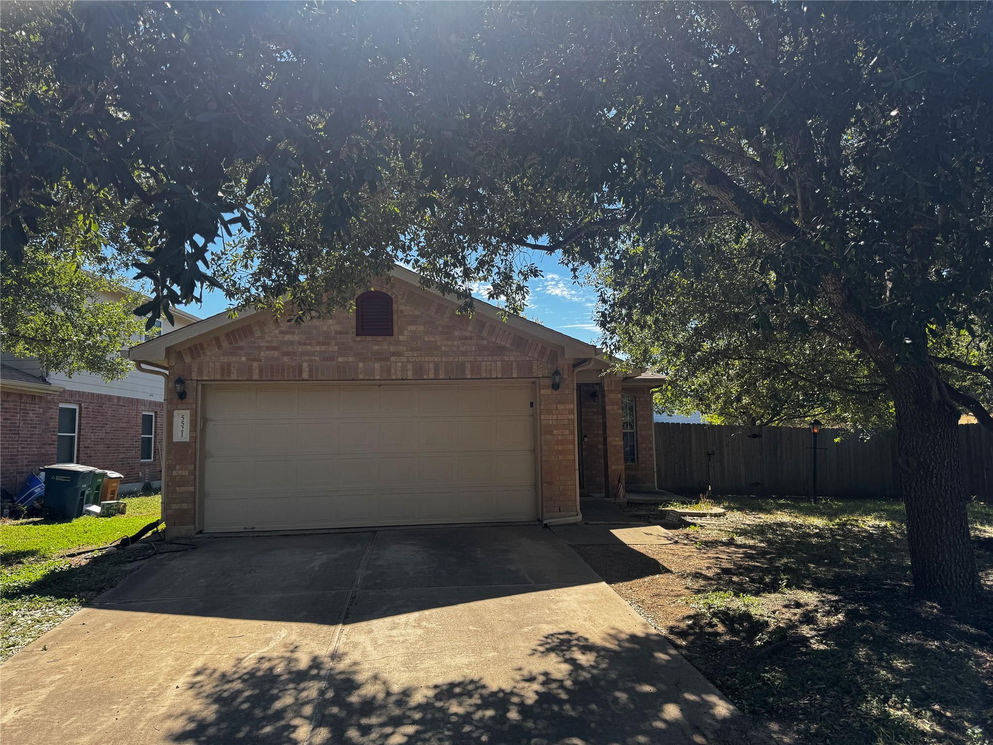 Mature trees shade the concrete driveway and bric