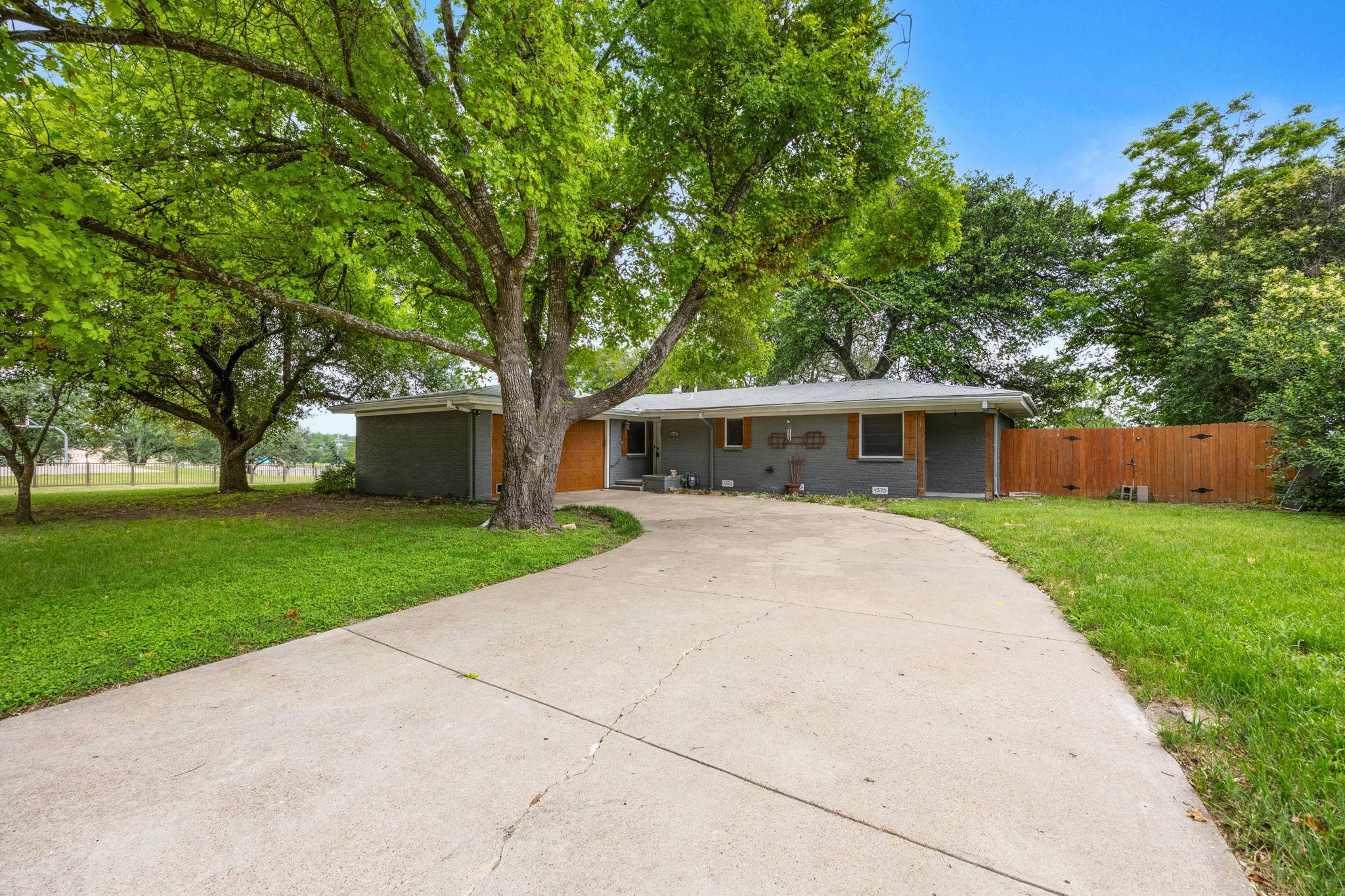 Mature shade trees frame a spacious concrete driv