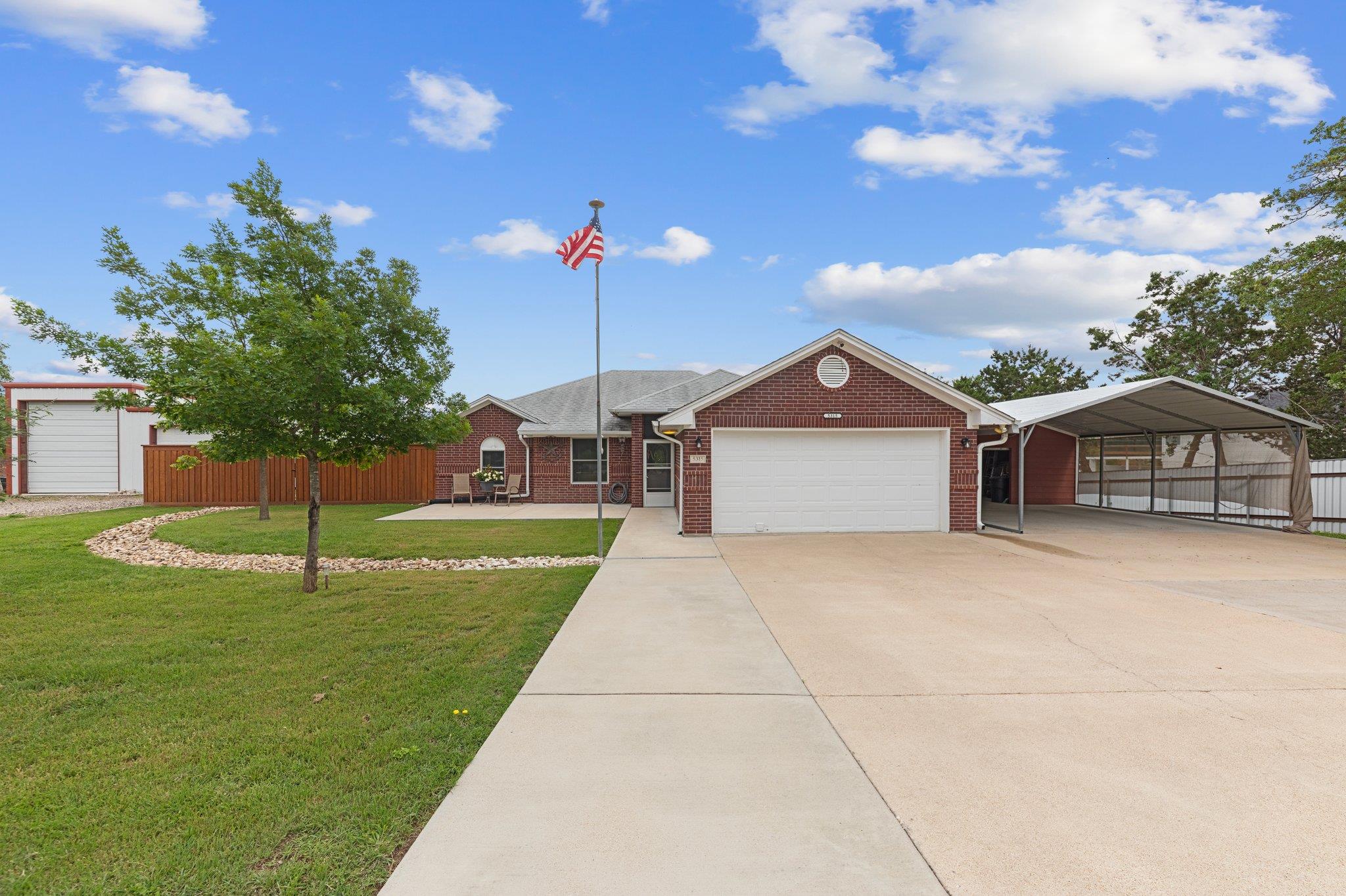 A wide concrete driveway leads toward the brick f