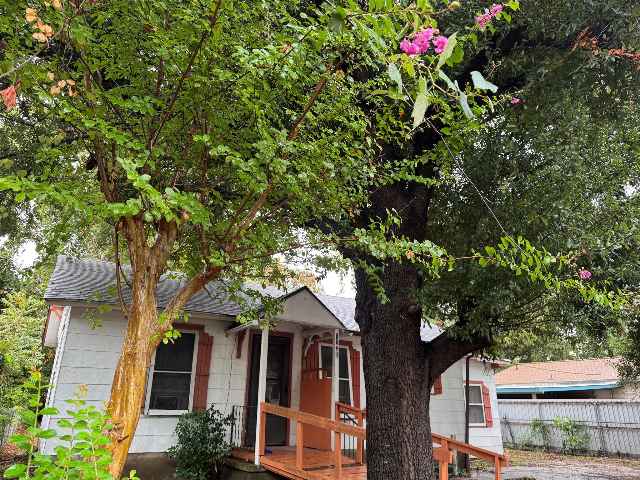 Mature trees shade the front entrance and wooden 