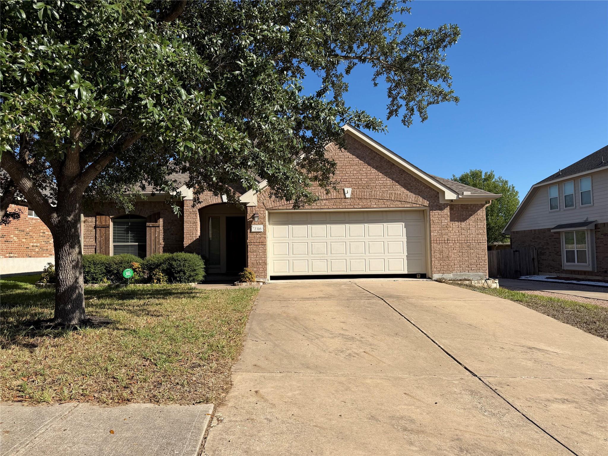 Mature shade trees flank the concrete driveway le