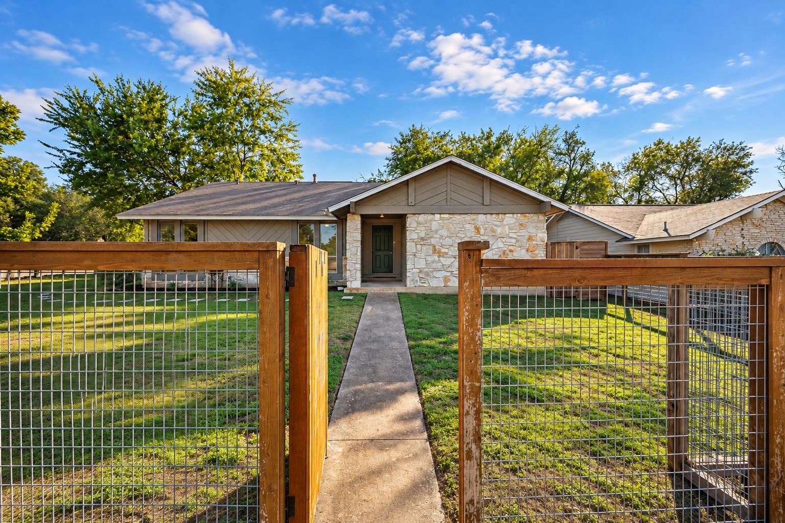 A concrete walkway leads through a fenced front l