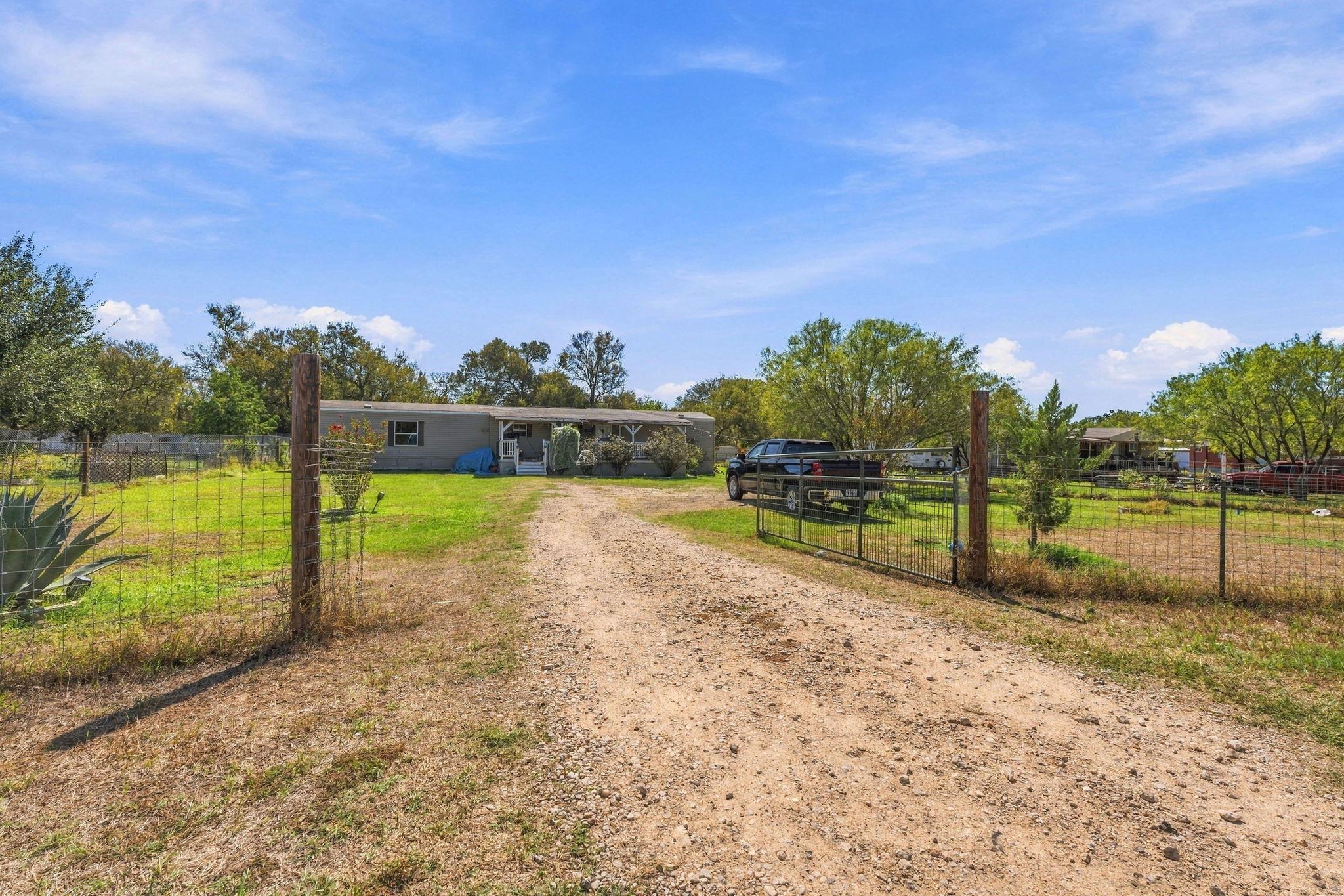 A long unpaved driveway leads past fenced pasture
