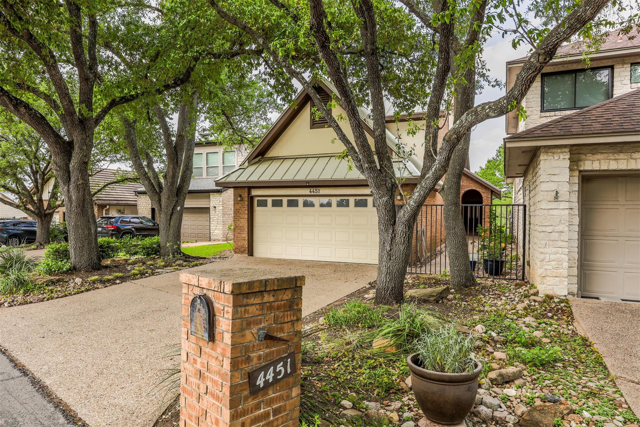 Mature trees shade the concrete driveway and ston