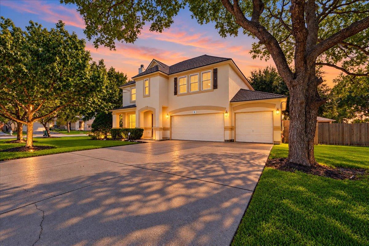 Mature trees frame the concrete driveway of a cla