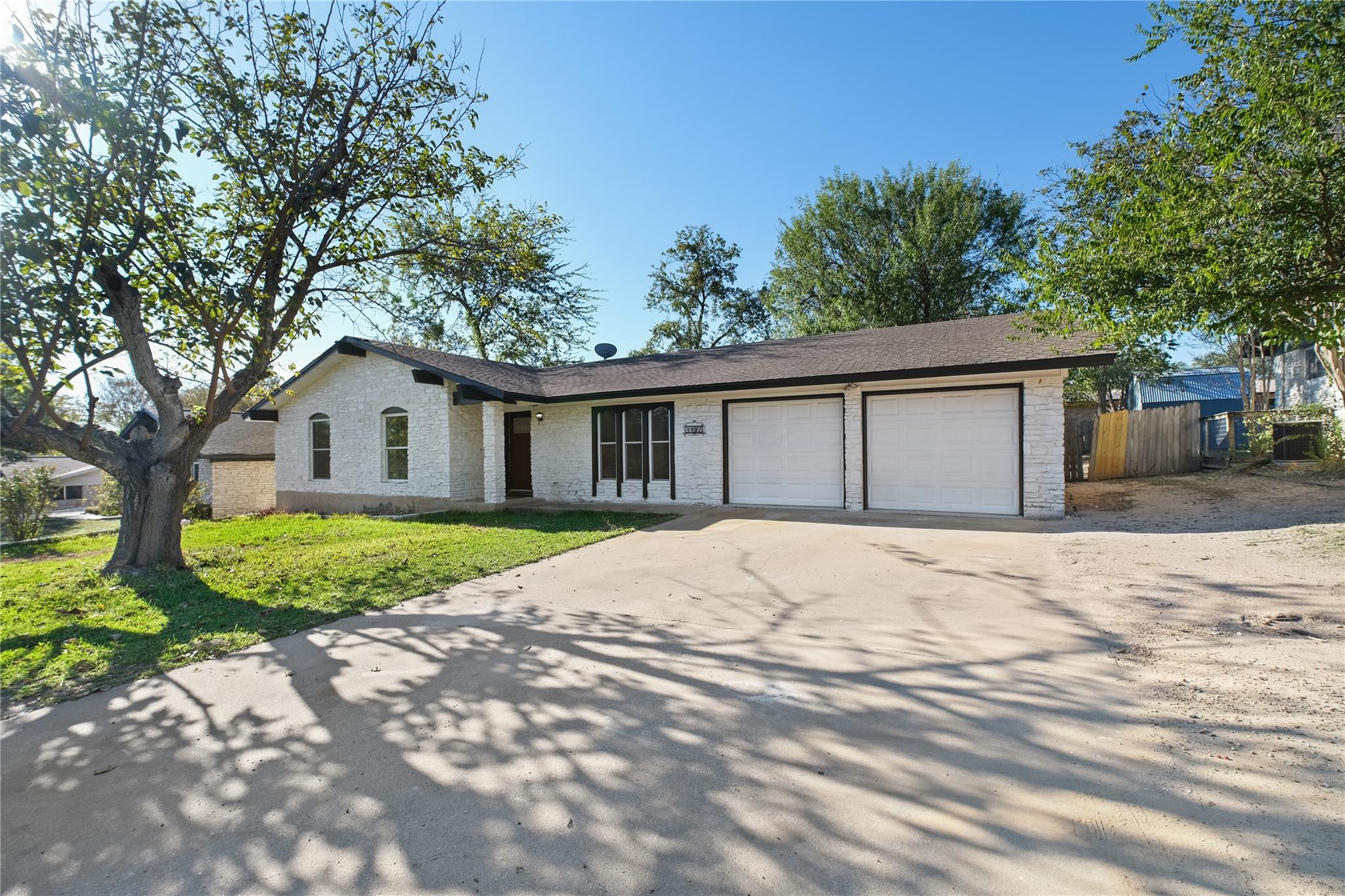Mature trees shade the wide concrete driveway lea