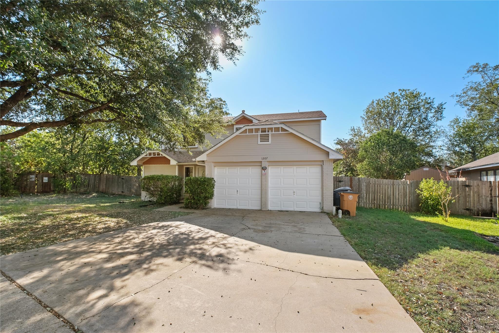 Mature trees shade a wide concrete driveway leadi