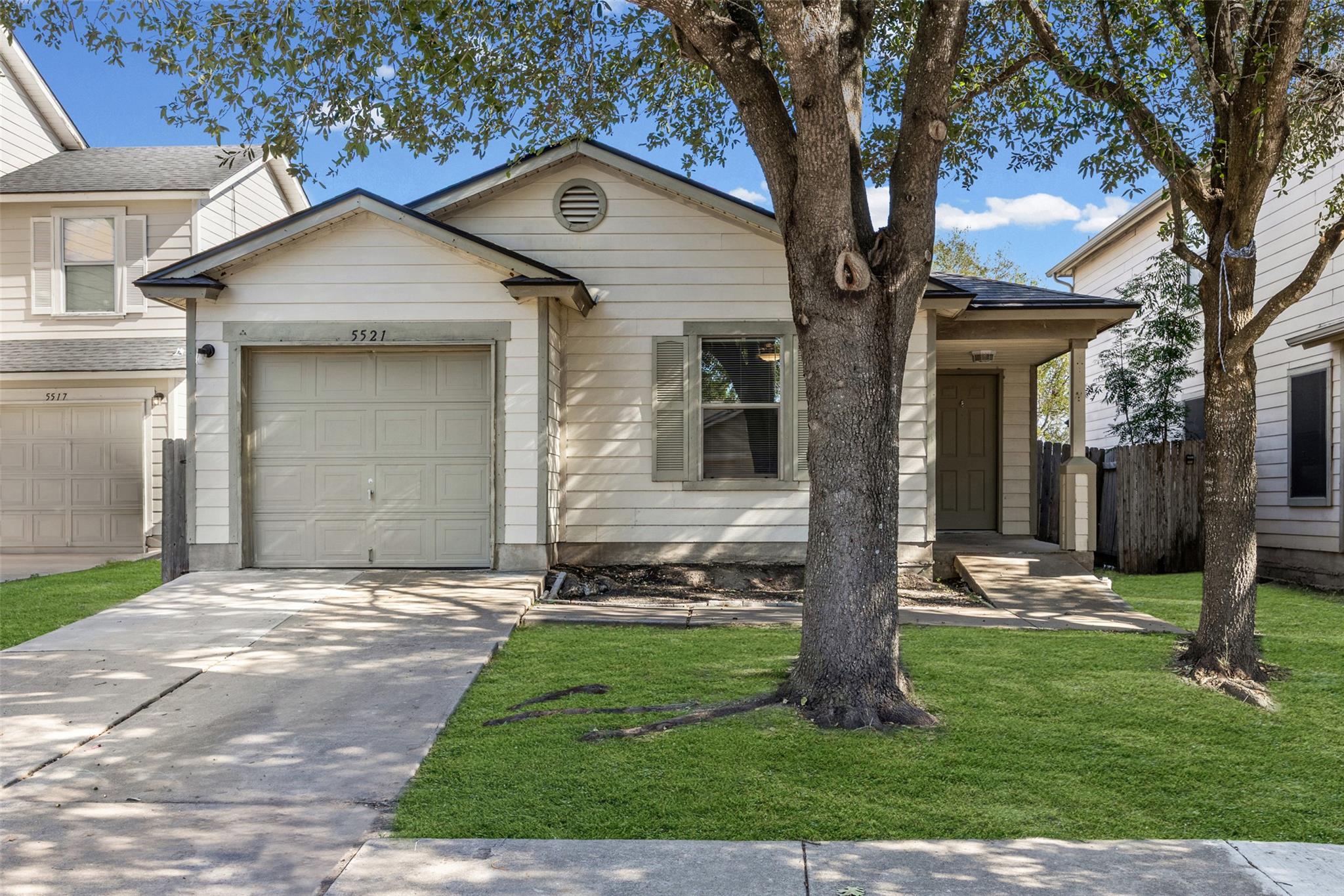 Mature trees shade the concrete driveway and neat