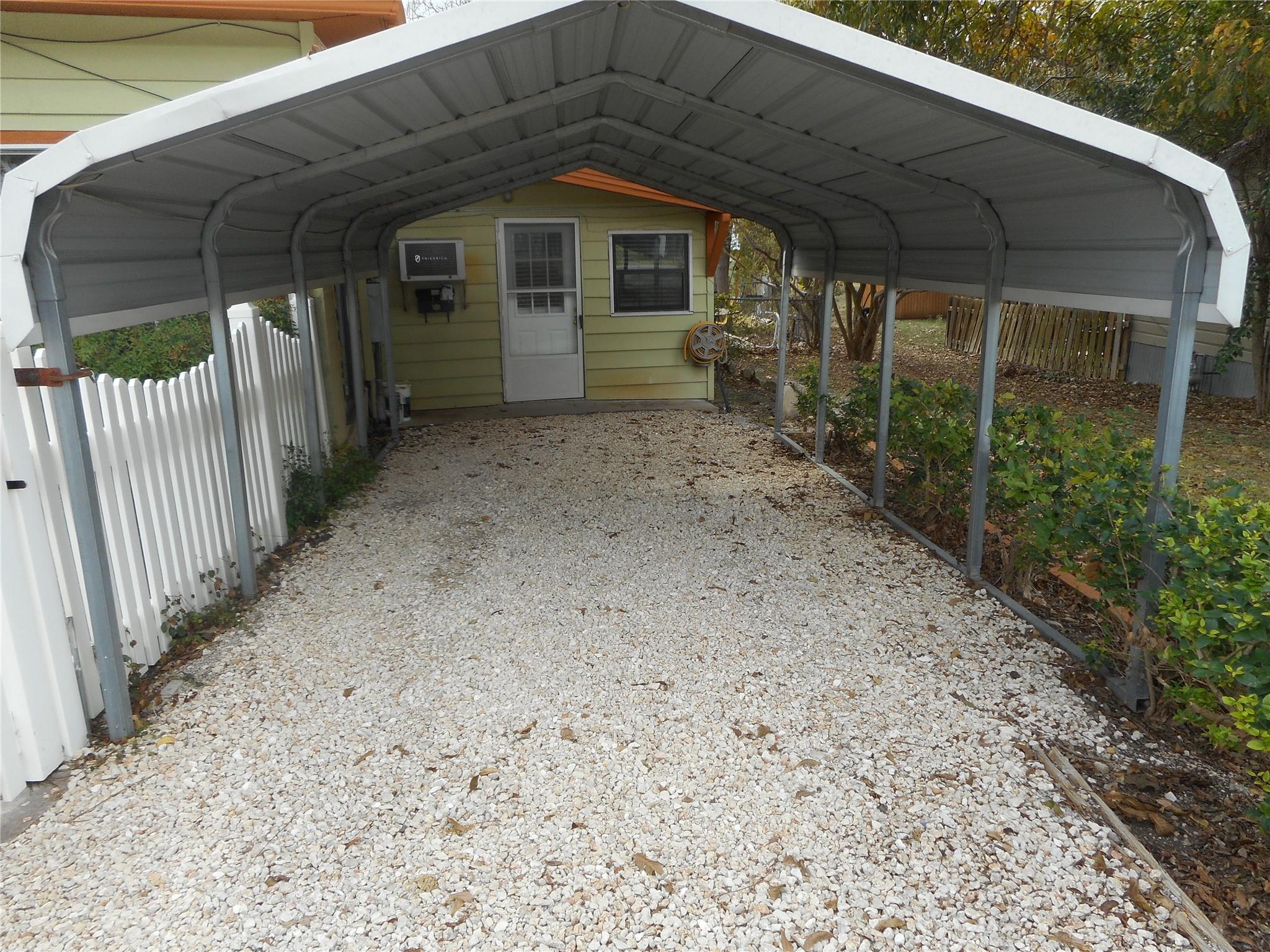 A spacious covered metal carport features a grave